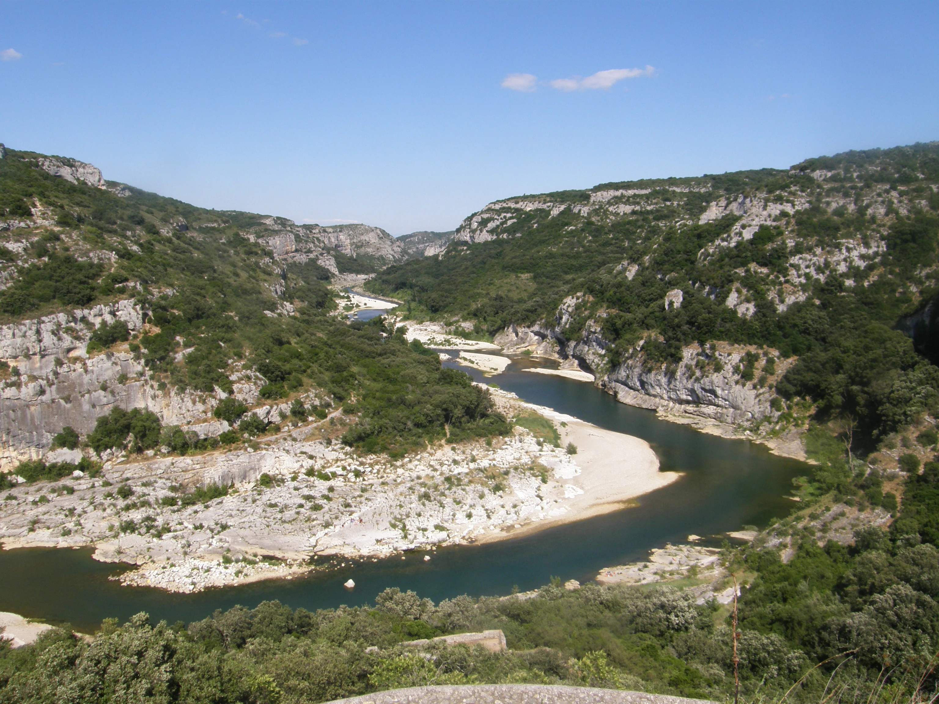 A high angle shot looking down into a deep river canyon with limestone cliffs, scrubby vegetation, and a winding river with gravel banks.
