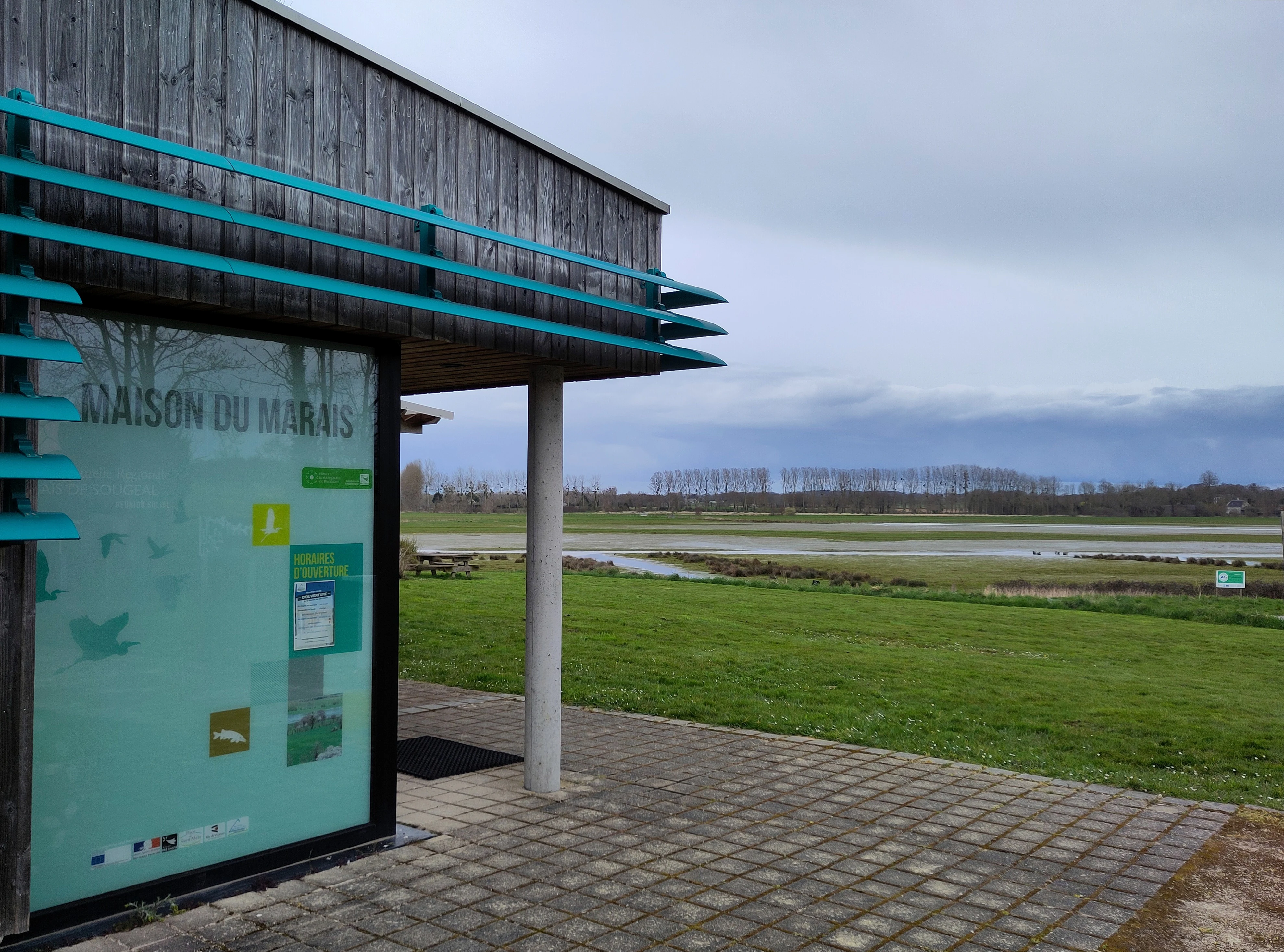 Exterior view of the Maison du marais visitor center building with its turquoise accents, situated at the edge of the open wetland marsh landscape.