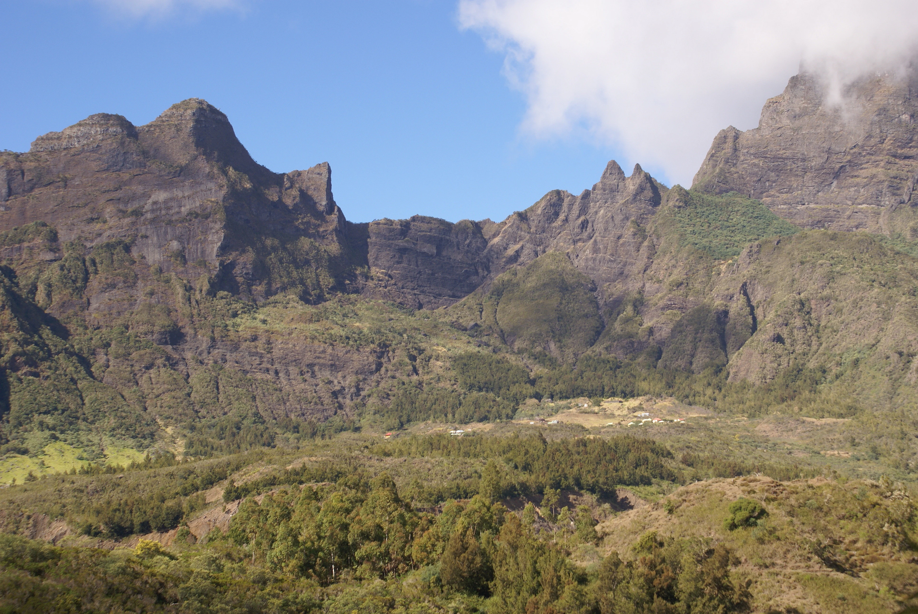 Panoramic view of steep volcanic mountain peaks with green valleys and scattered vegetation under a partly cloudy sky