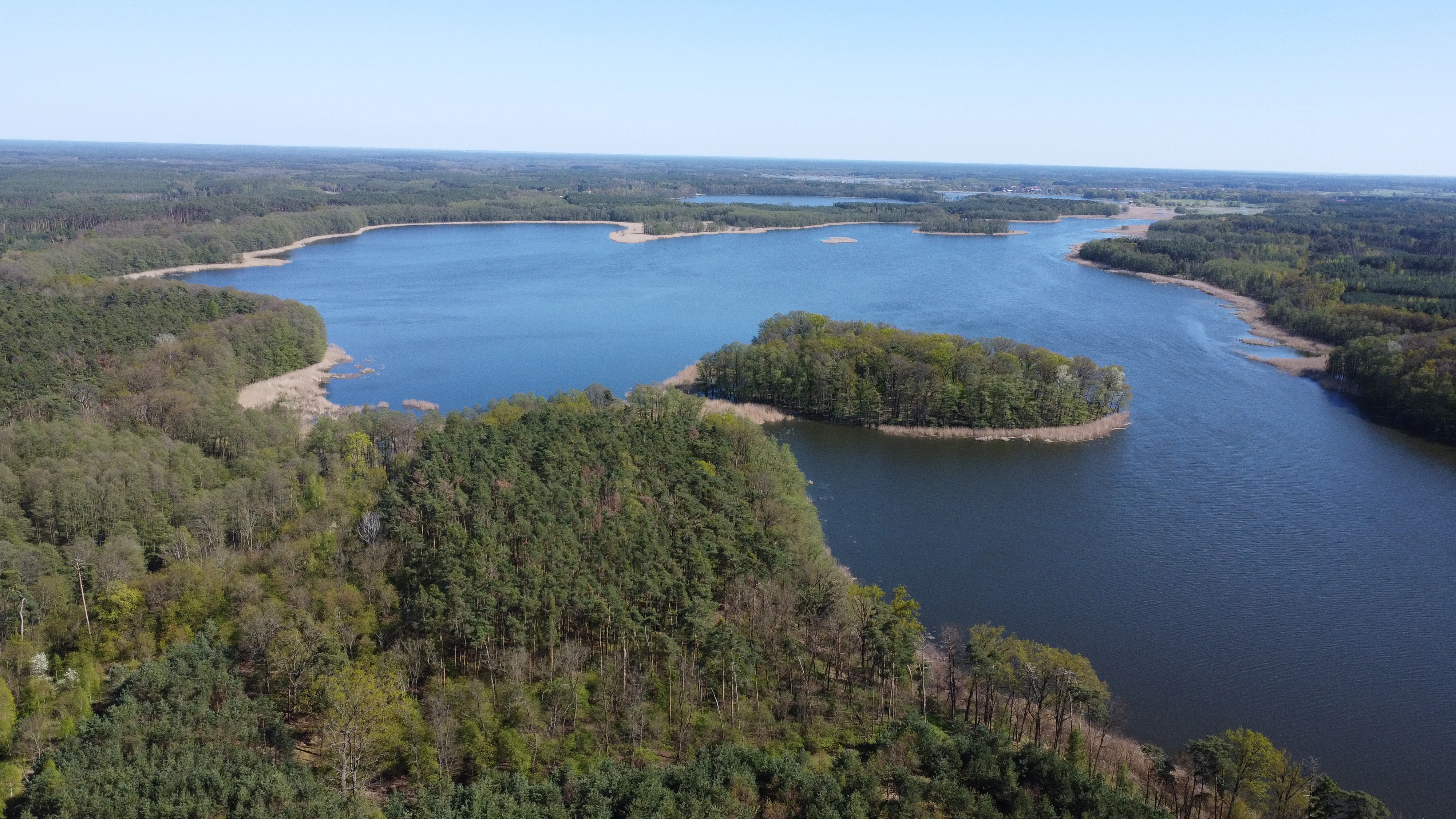 An aerial view of a large, blue lake surrounded by dense green forest in Poland.