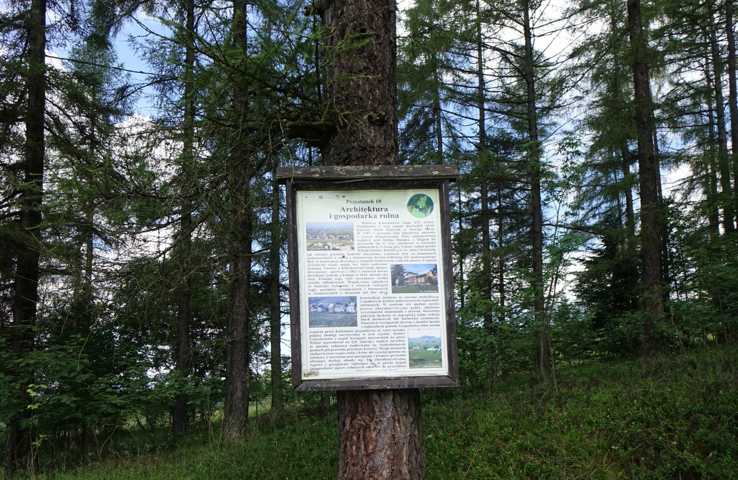 A rectangular information board mounted on a large tree trunk in a forested area, featuring text and small photographic inserts about the nature reserve.