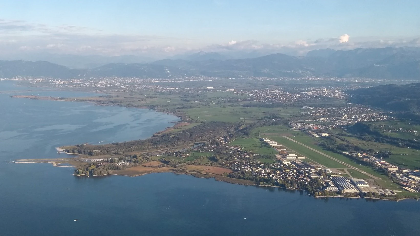 Wide aerial photograph of the Rhine Delta on the edge of Lake Constance, showing water, marshland, and a nearby runway.