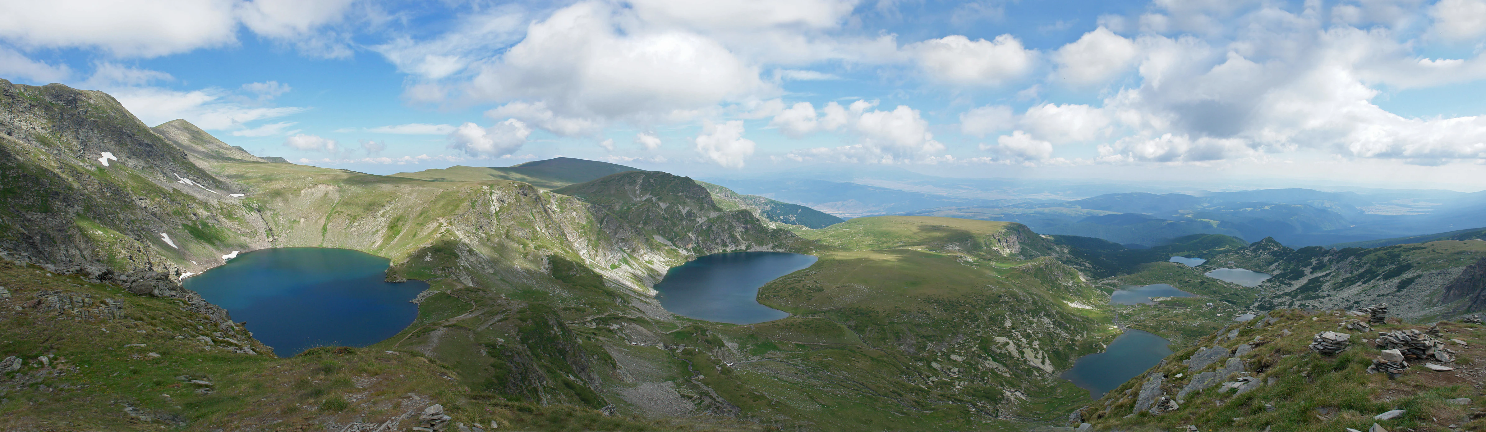 Panoramic view of seven alpine lakes surrounded by mountain slopes under a partly cloudy sky