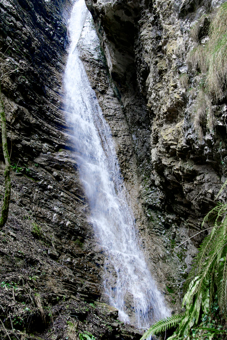 Una cascada estrecha que cae por la pared rocosa y escarpada de un desfiladero en un cañón angosto.