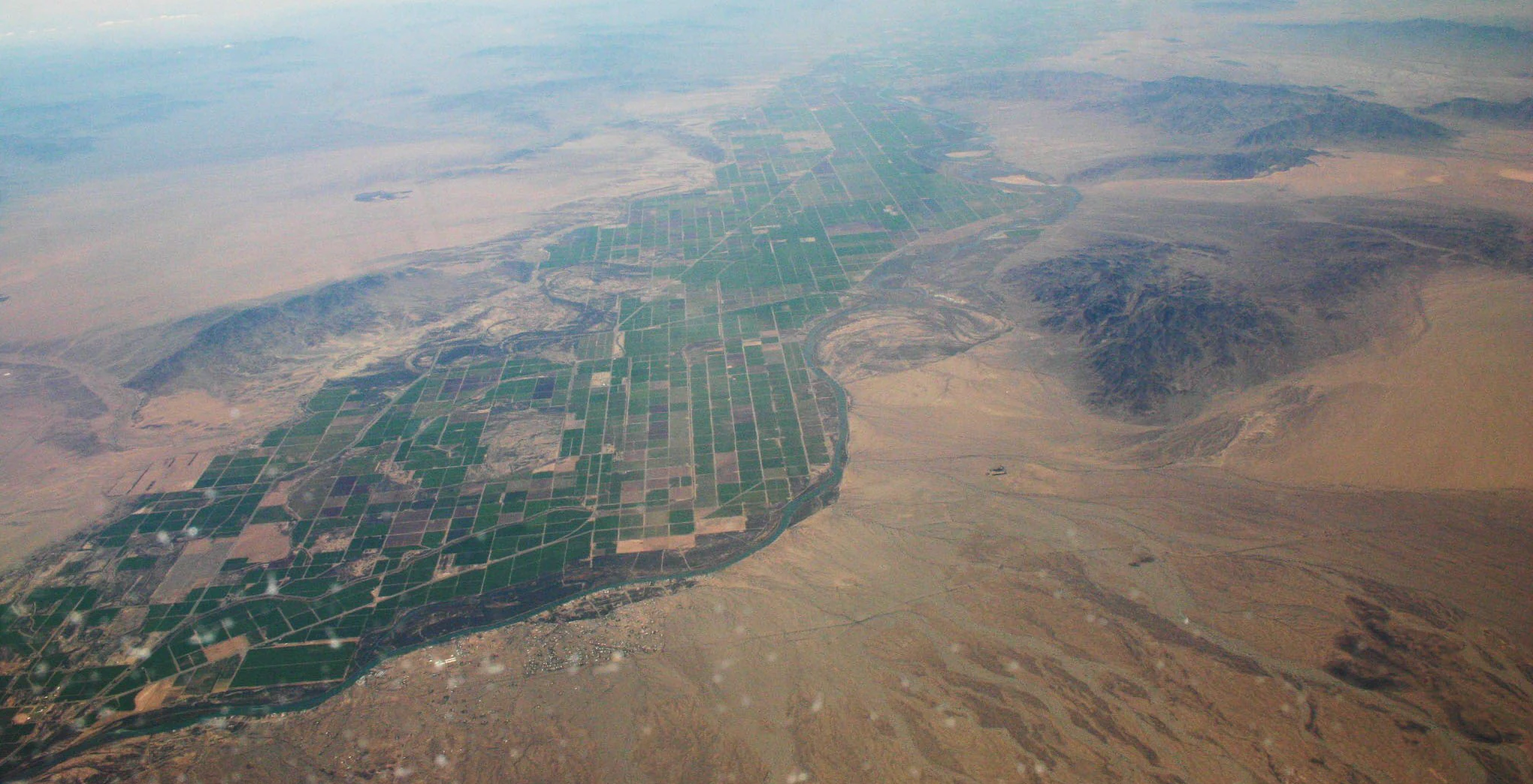 Vista aérea oblicua mirando al sur sobre el valle de Parker, que muestra un marcado contraste entre los campos agrícolas verdes y el paisaje desértico marrón circundante.