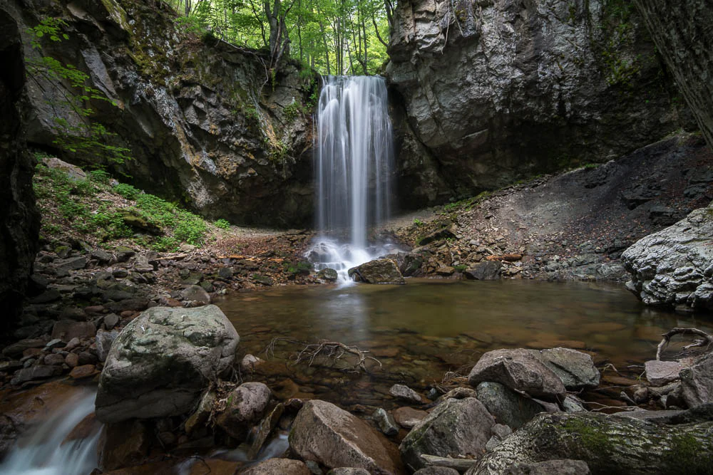 Waterfall cascading over rocks into a pool surrounded by forest and boulders