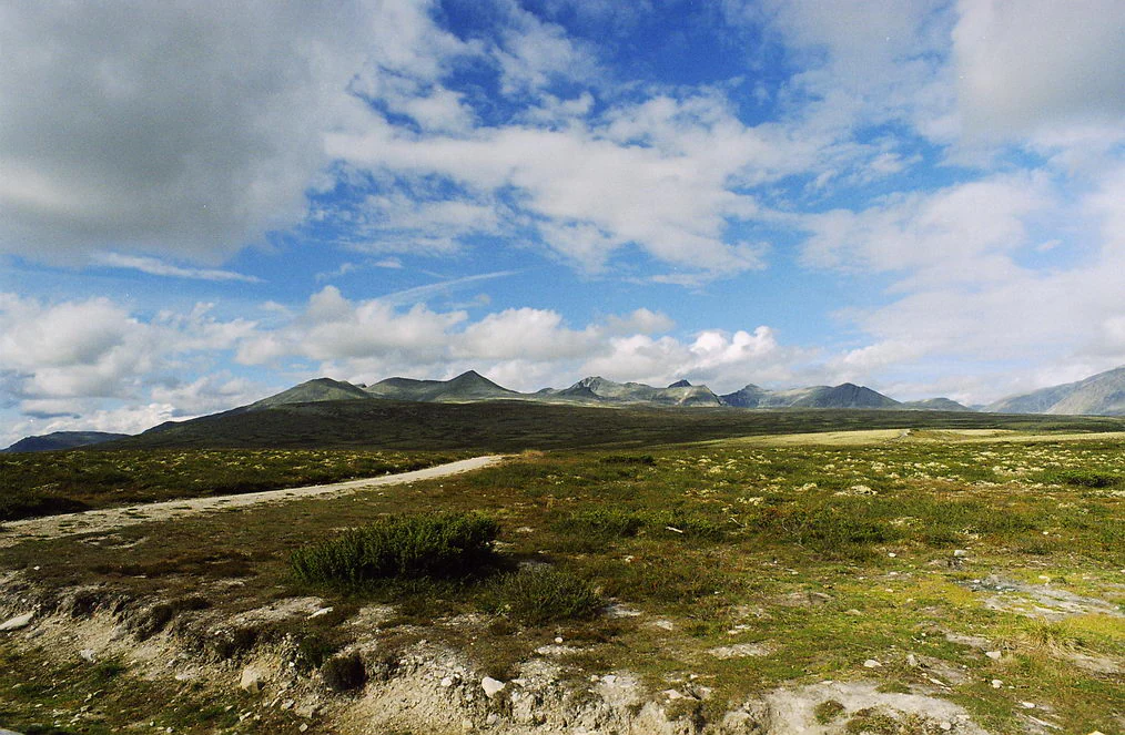Wide view of open tundra landscape with distant mountain peaks under partly cloudy sky