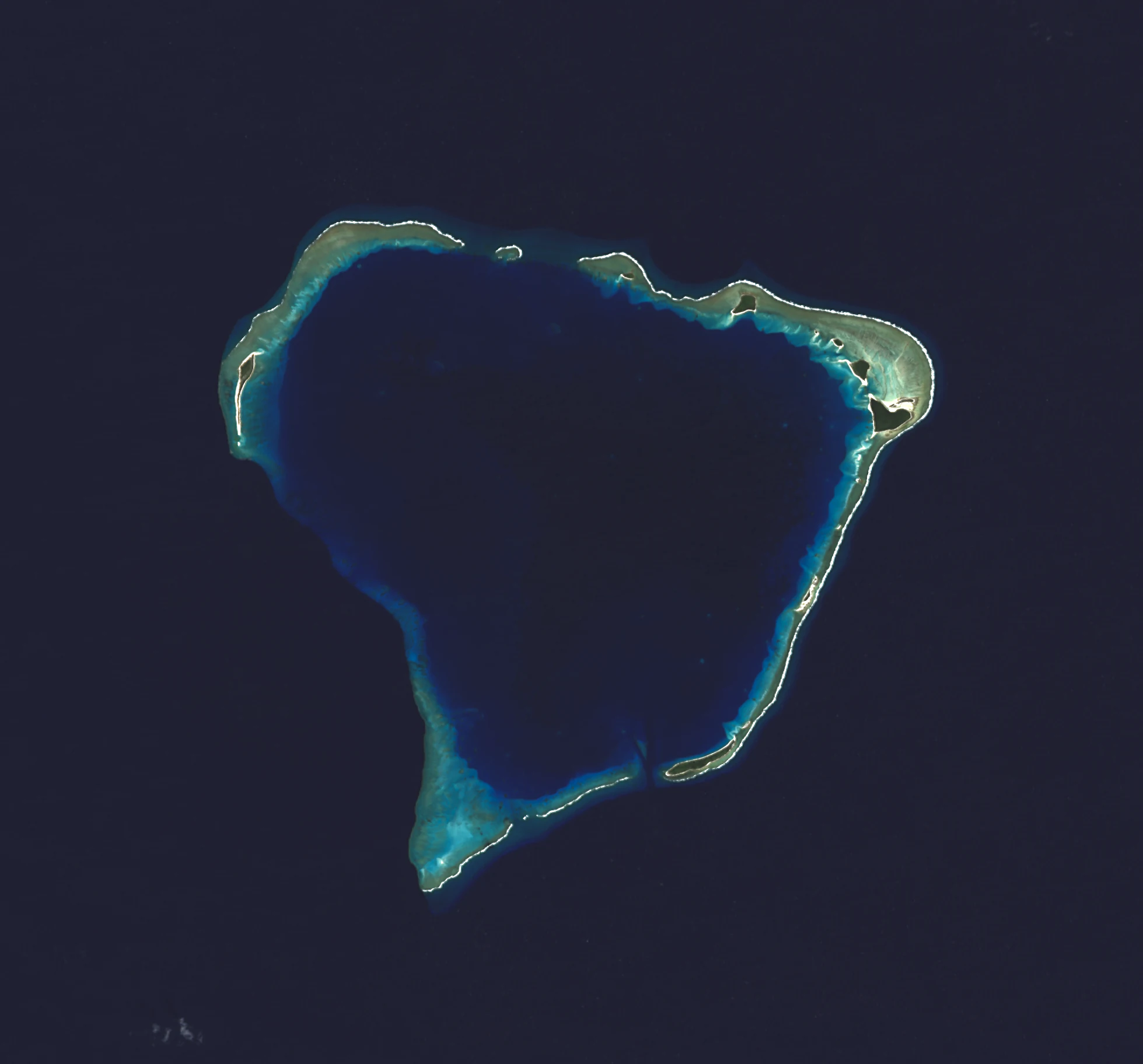 Top-down satellite view of a coral atoll featuring a central deep blue lagoon surrounded by a ring of small sandy islets and coral reef structures against a dark ocean background.