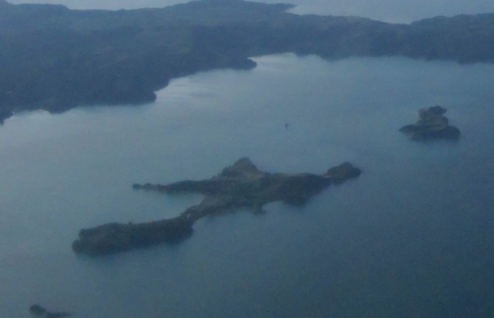 An aerial perspective of Rotoroa Island surrounded by ocean, showing its irregular shape and grassy landscape.