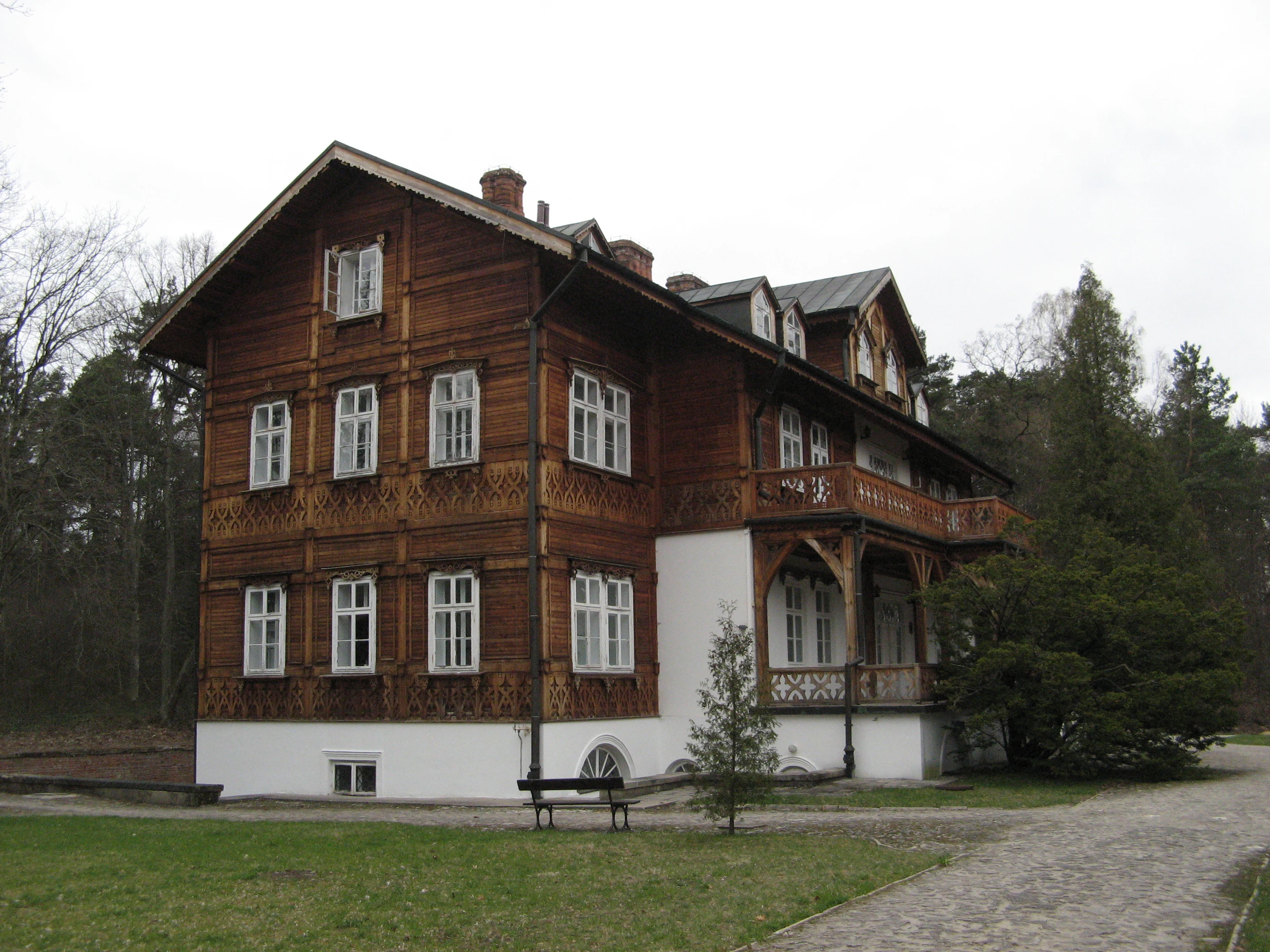 A large wooden house with white trim and multiple windows, situated on a grassy area with a pathway and trees in the background