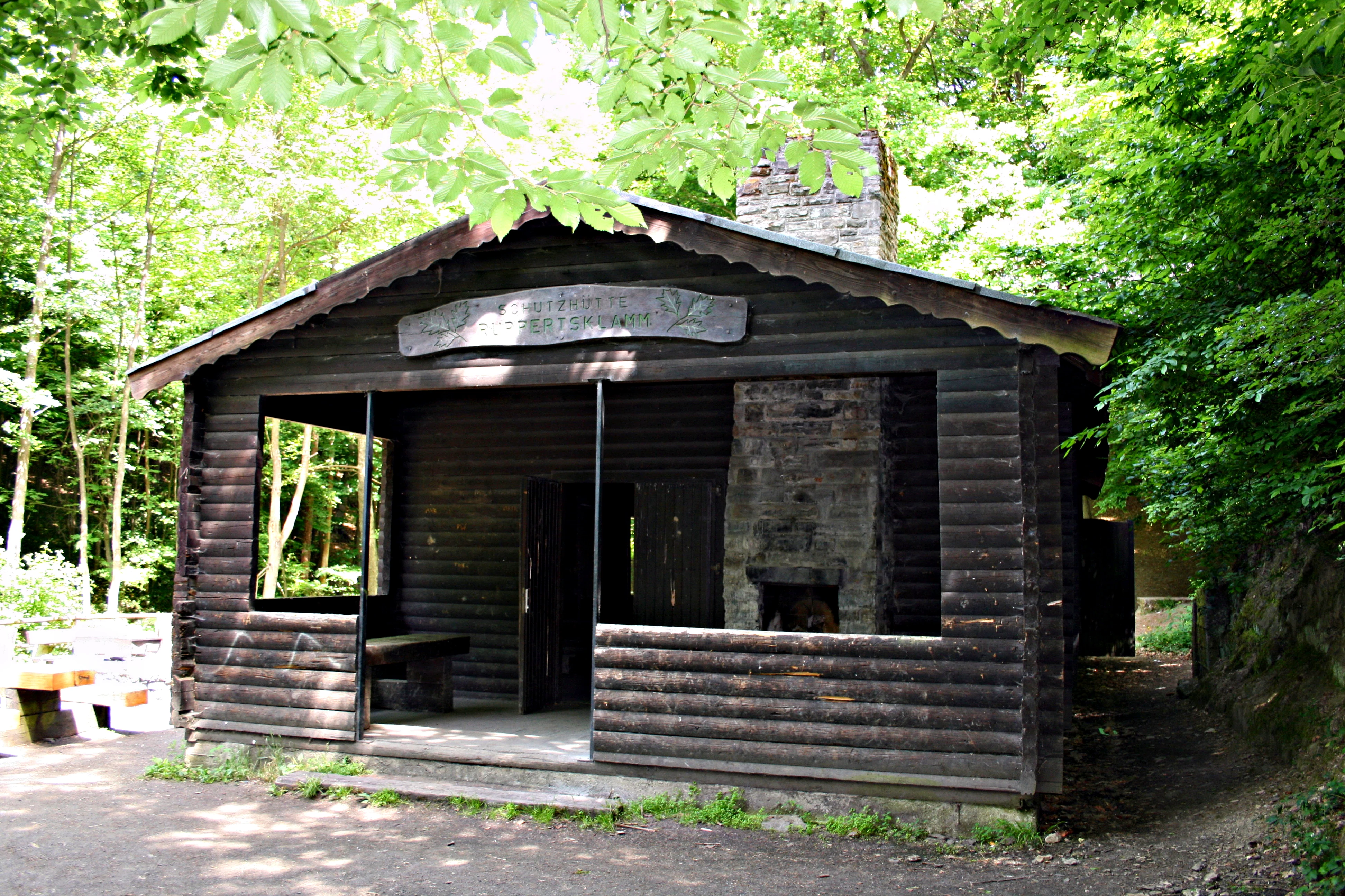 A rustic wooden shelter with a stone chimney nestled in a forest.