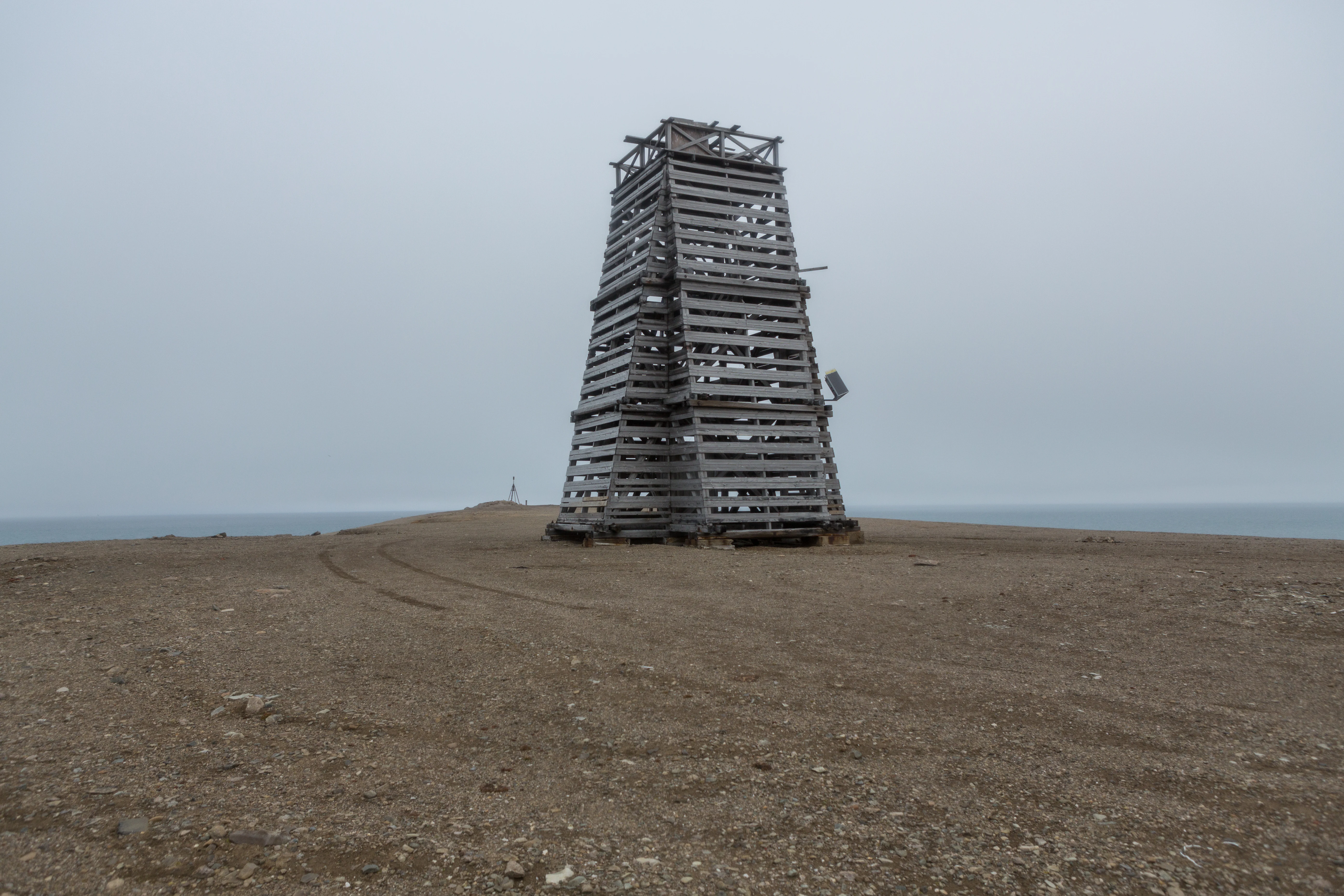 Tall wooden tower structure on a rocky coastal plain with the sea in the background under an overcast sky