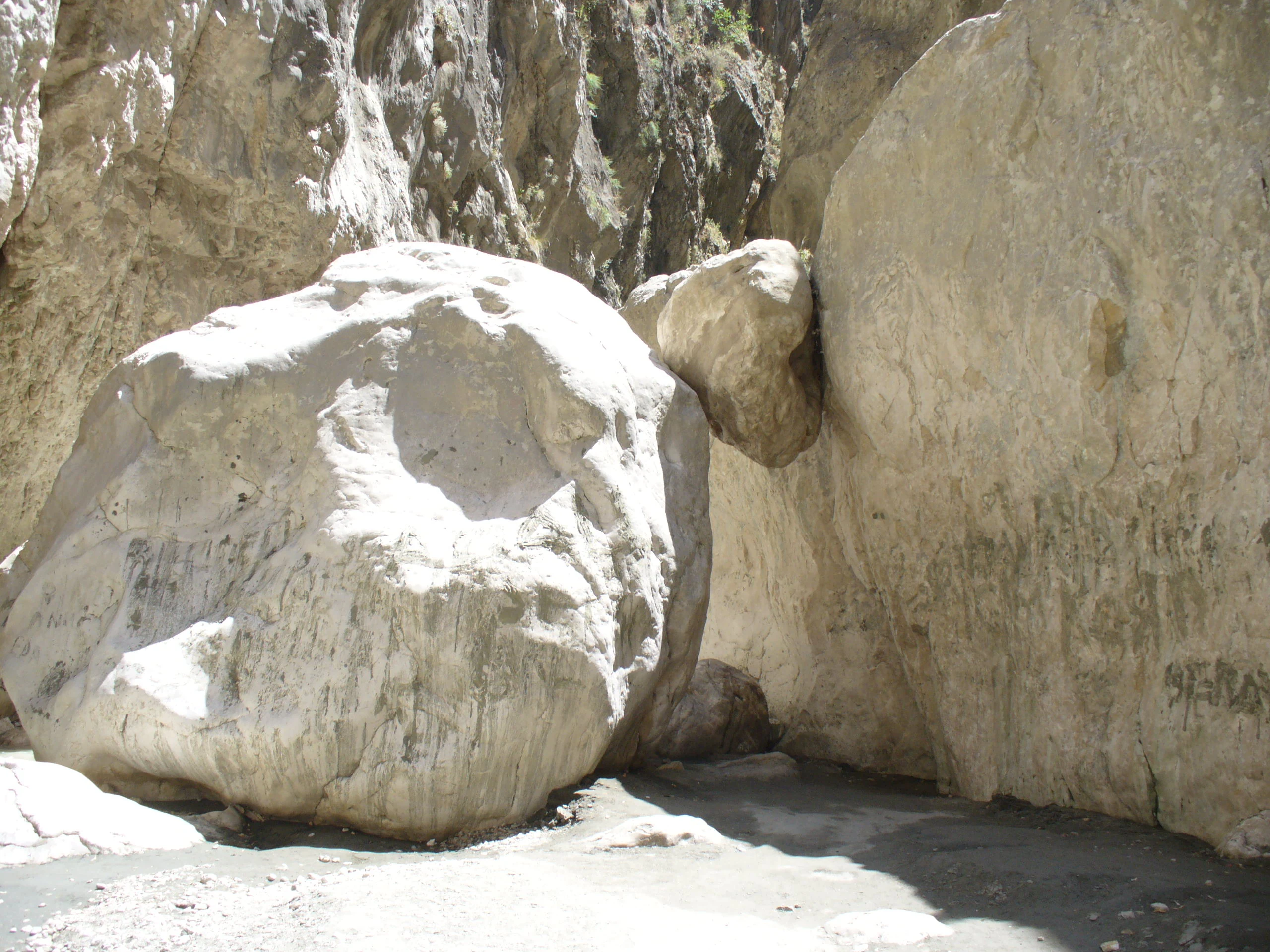 Large light-colored boulder surrounded by rocky canyon walls in a dry riverbed