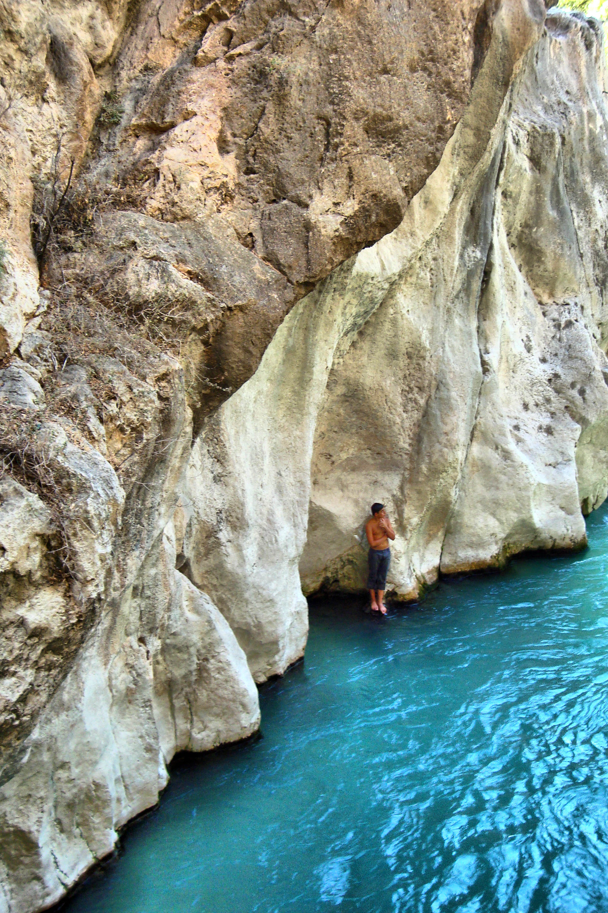 Person standing on a rock ledge beside a turquoise river in a canyon with steep rocky walls