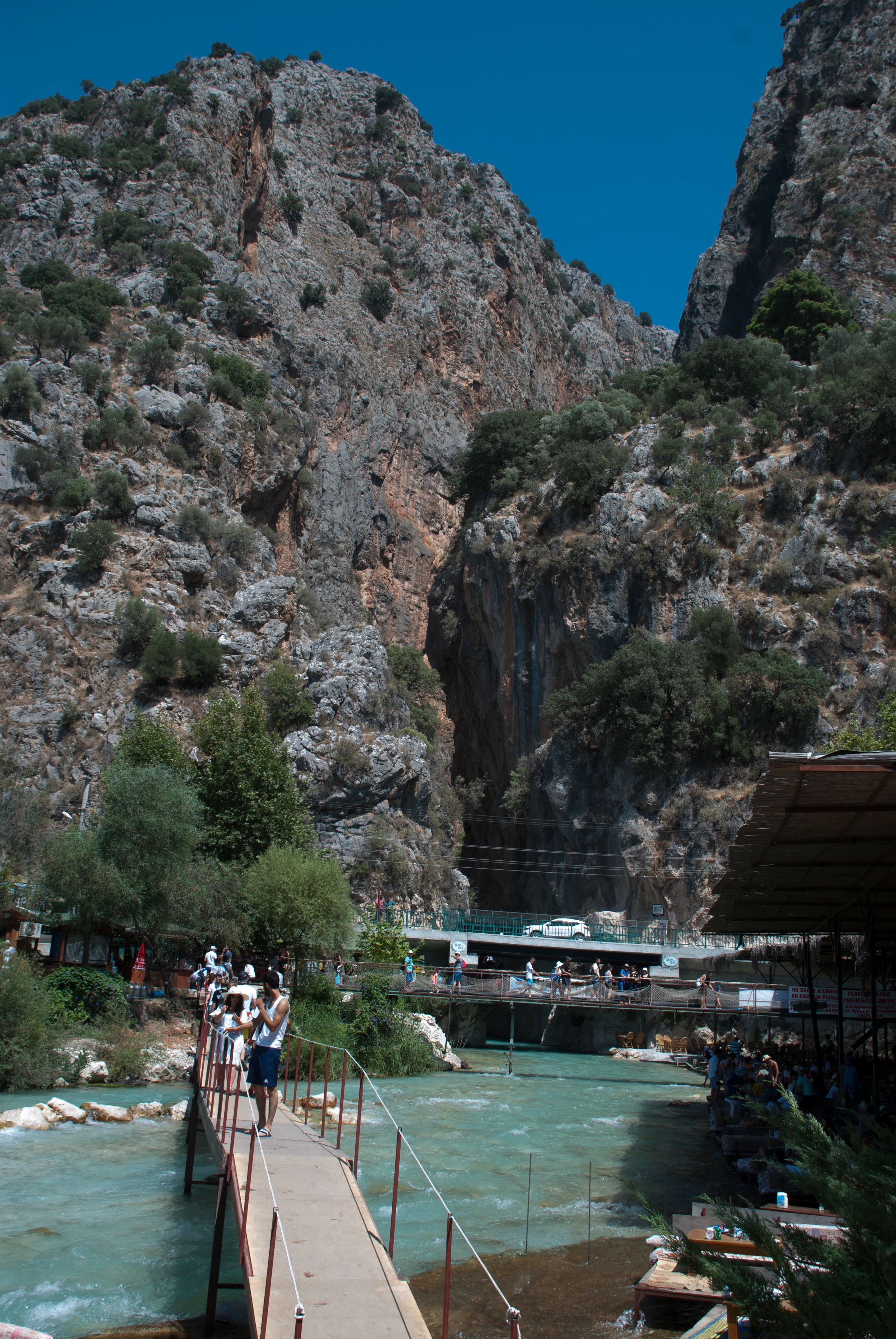 Pedestrian bridge crossing turquoise river in deep canyon with rocky cliffs and vegetation