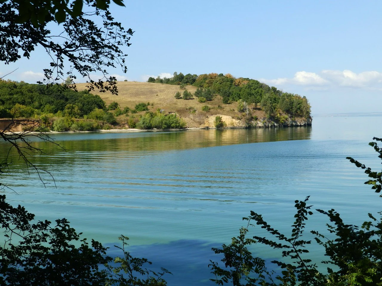 Landscape view of calm blue water with hills and vegetation on the shore under a clear sky
