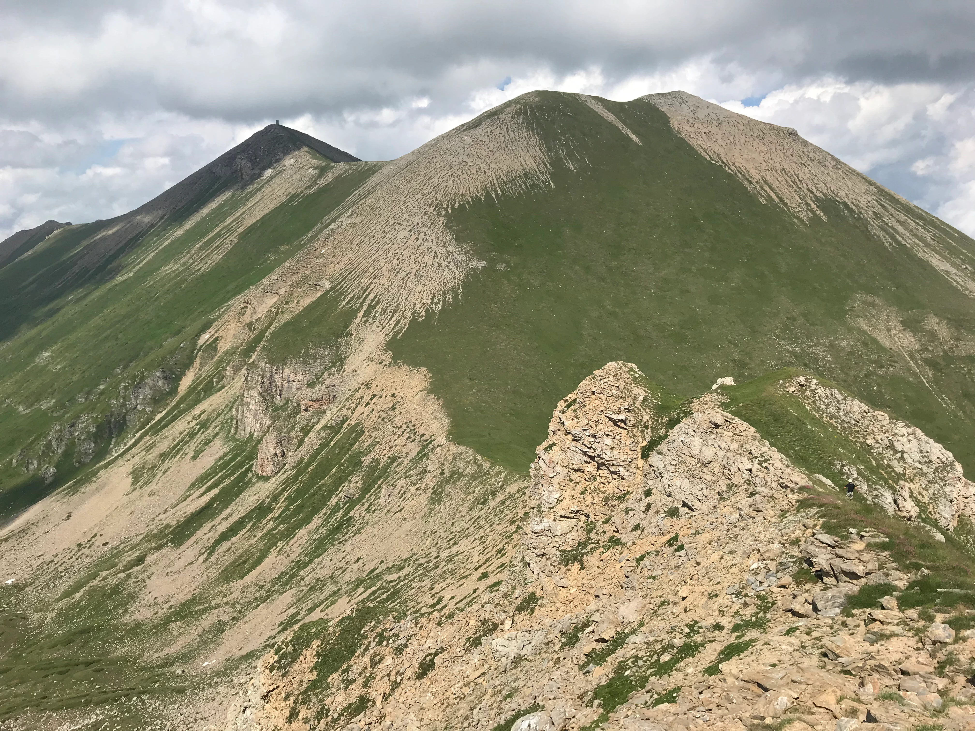 Two prominent mountain peaks with rocky slopes and green vegetation under a partly cloudy sky
