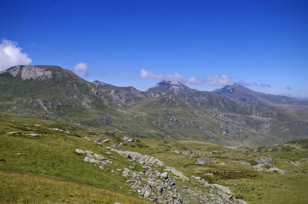 Grassy and rocky mountain slopes with distant peaks under a clear blue sky