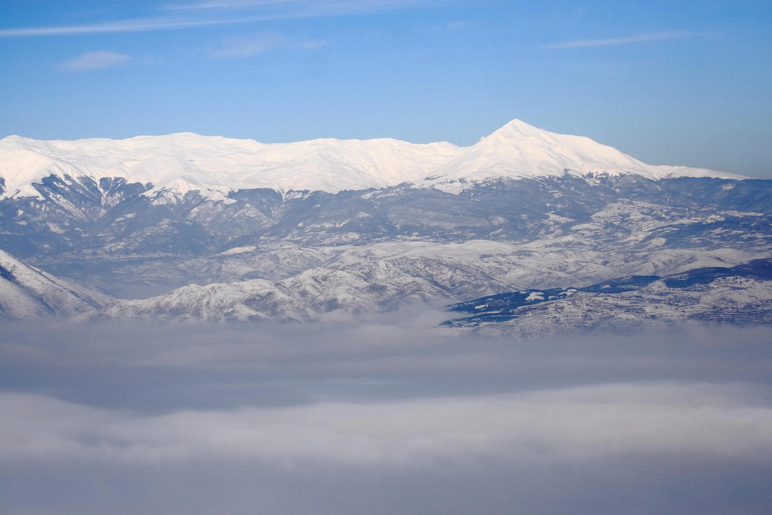 Wide aerial view of snow-covered mountain peaks with clouds below