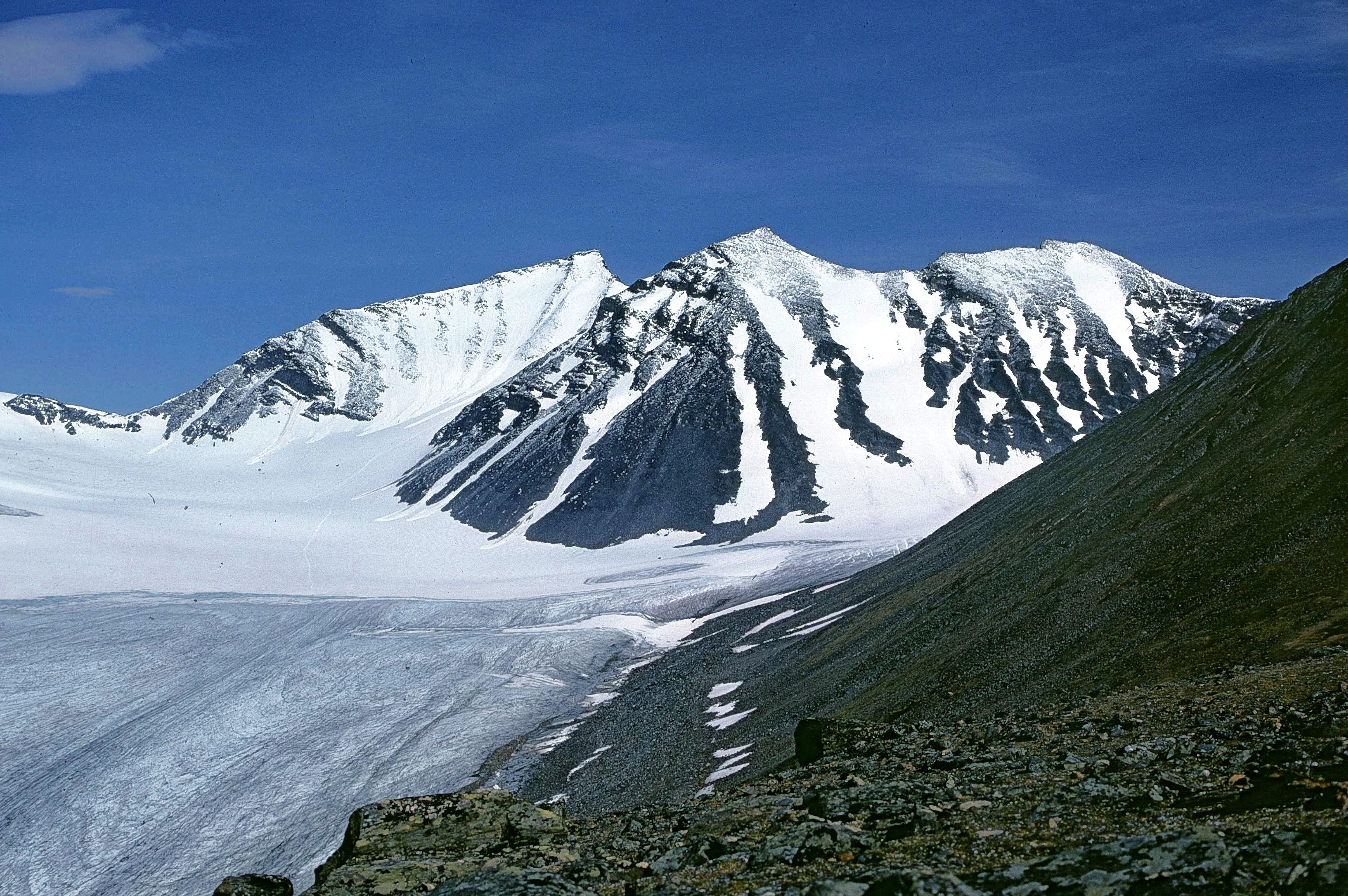 Snow-covered mountain peaks and glaciers in a mountainous landscape with rocky terrain in the foreground