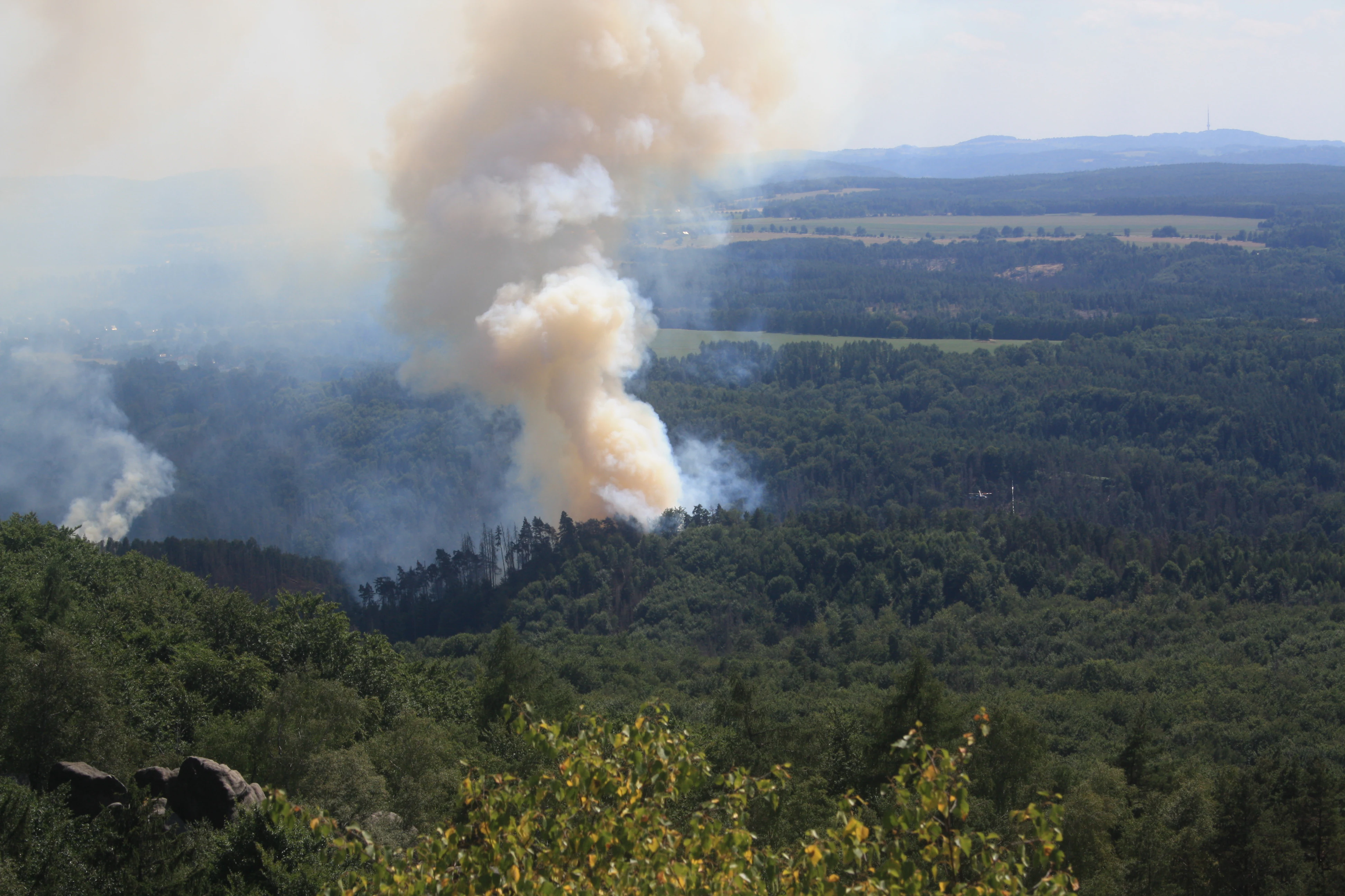 Forest fire with large smoke plume rising from wooded area in mountainous landscape