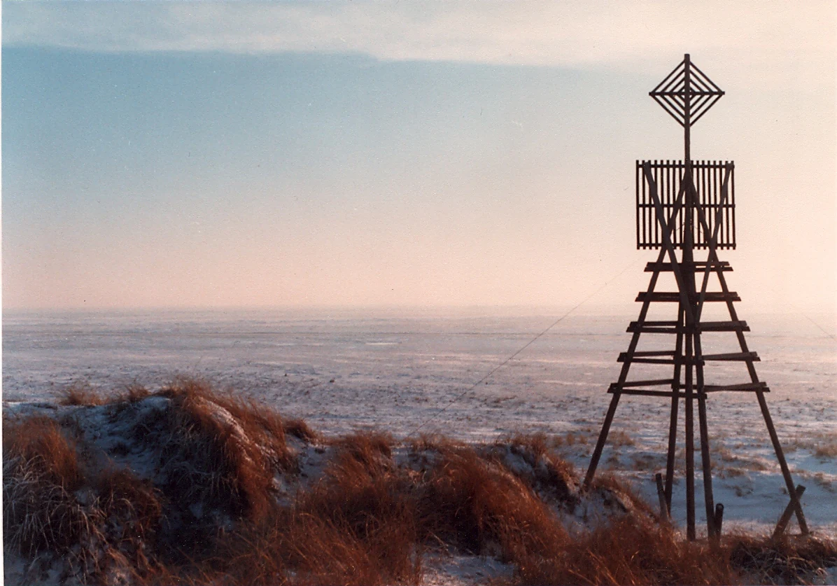 Triangulation beacon structure on sandy dune with coastal background