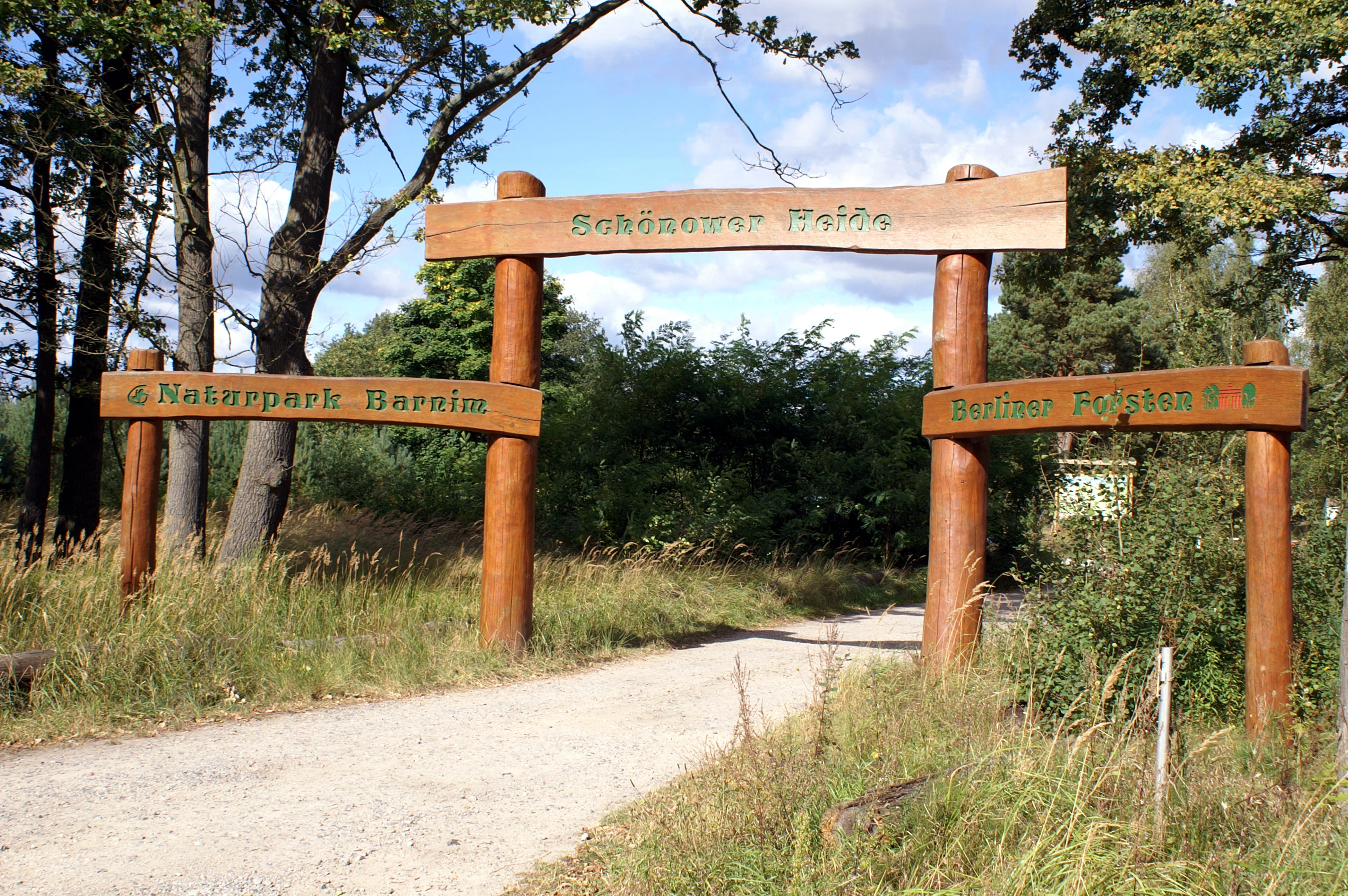 A rustic wooden archway serves as the entrance to the Schönower Heide nature reserve, with signs attached to the posts identifying the park and the Barnim Nature Park.