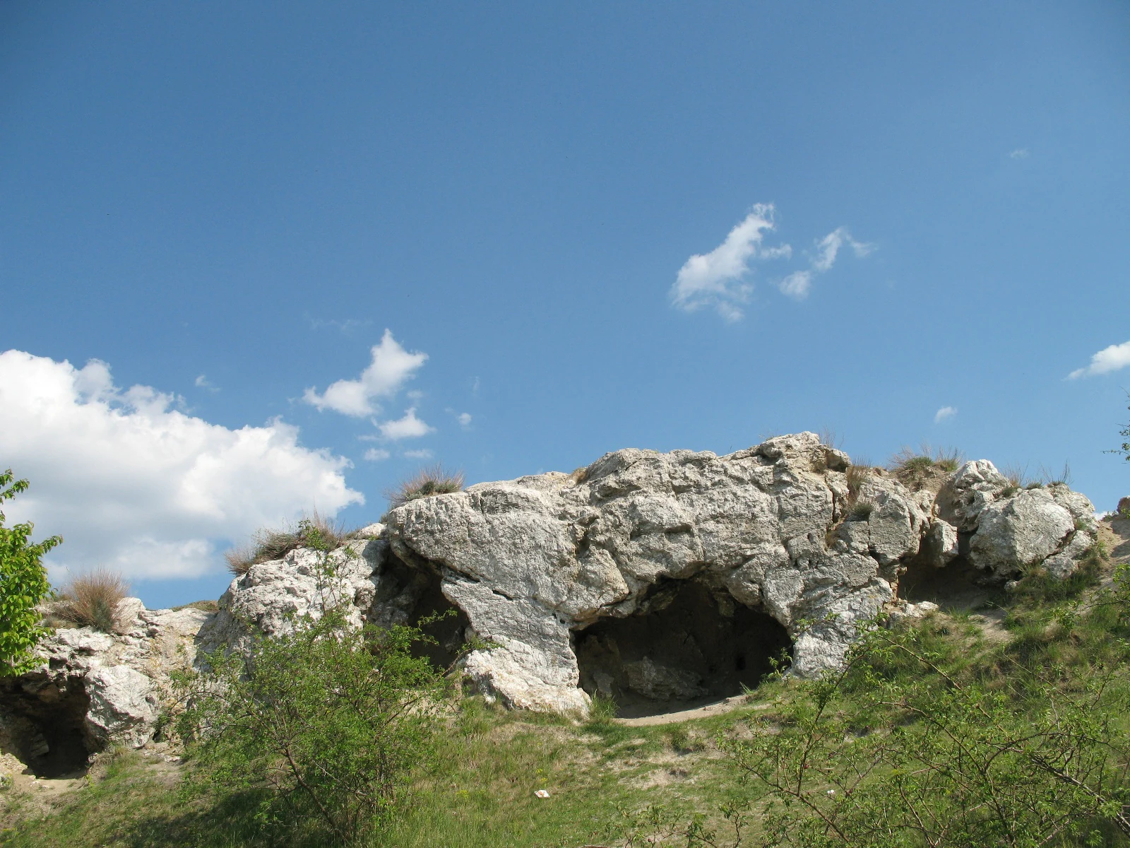 A low, weathered gypsum rock cliff face set into a grassy hill under a bright blue sky.