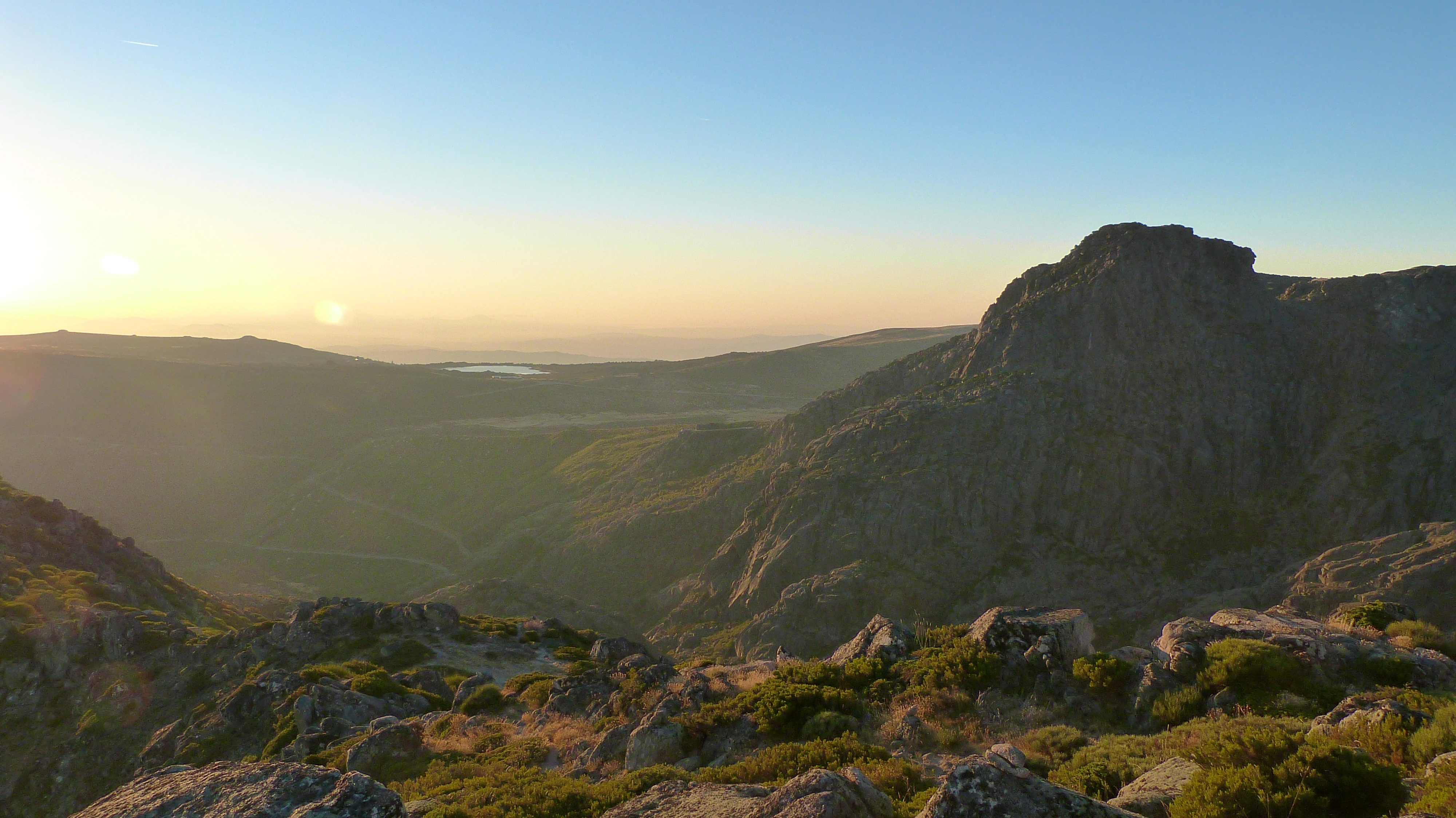Mountain plateau at dawn with rocky terrain, sparse vegetation, and a river valley under a clear sky
