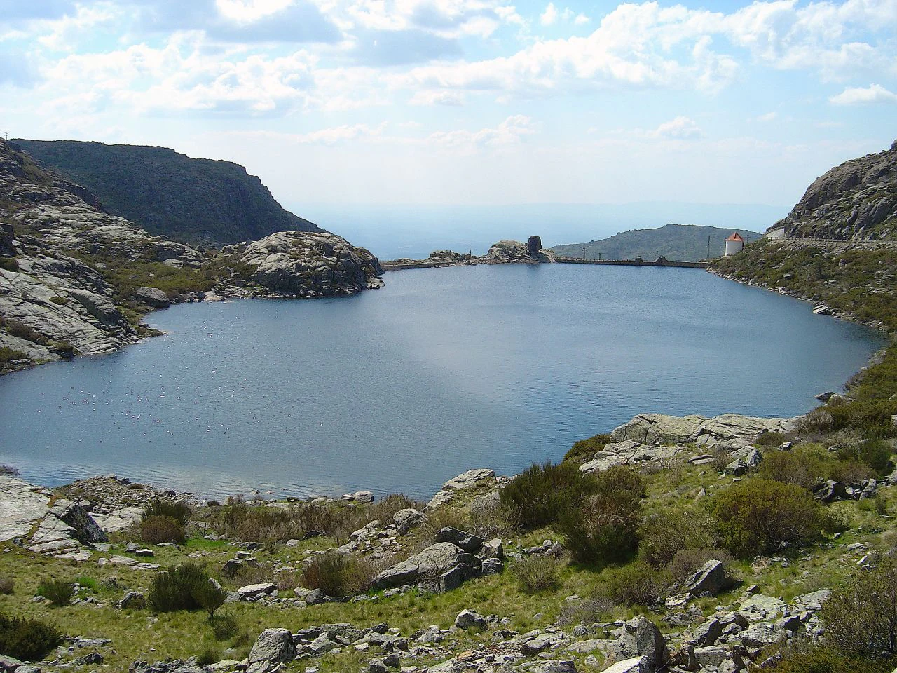 A large body of water surrounded by rocky hills and green vegetation under a partly cloudy sky
