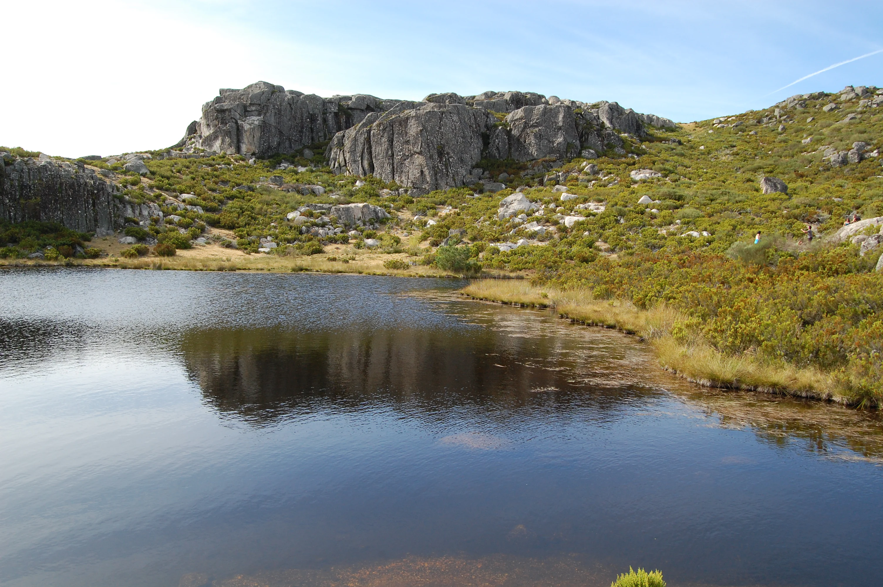 Calm lake reflecting rocky hills and green vegetation under a clear sky