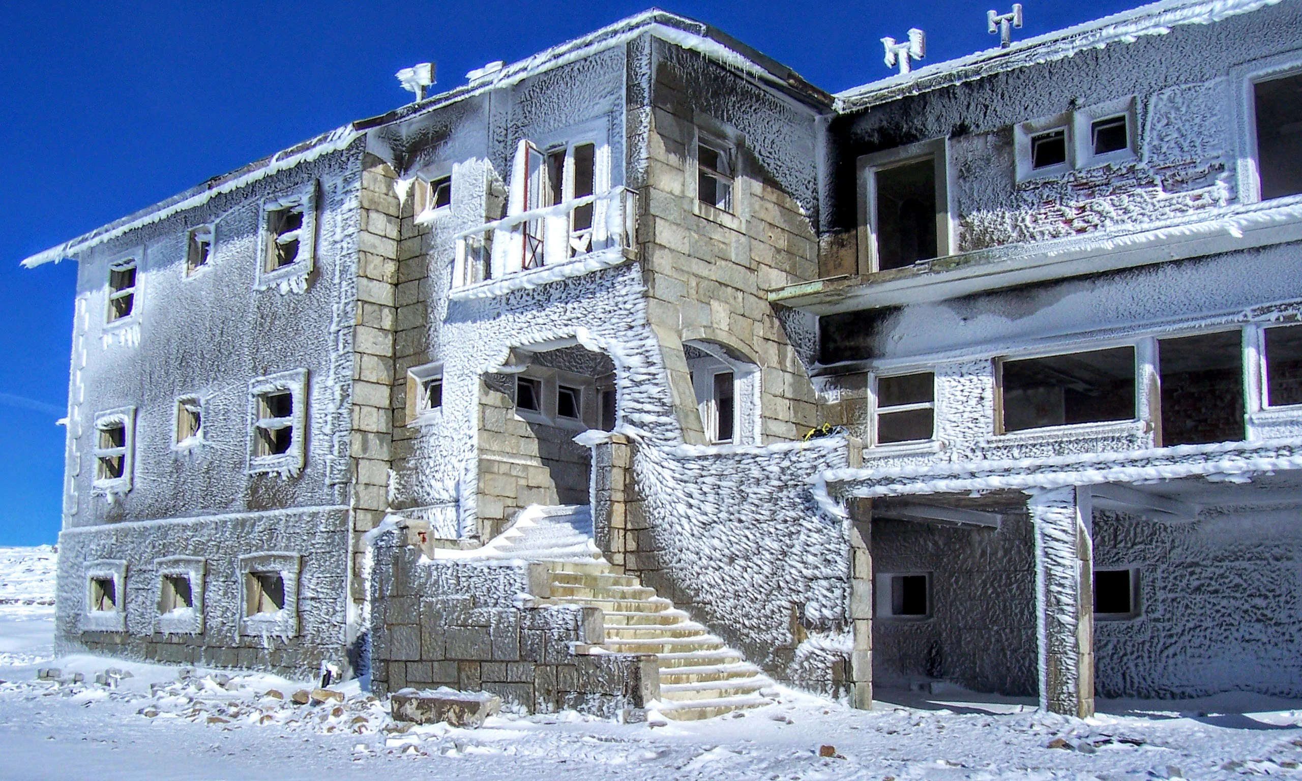 Abandoned stone building covered in ice and snow with missing windows and doors in a snowy mountain landscape