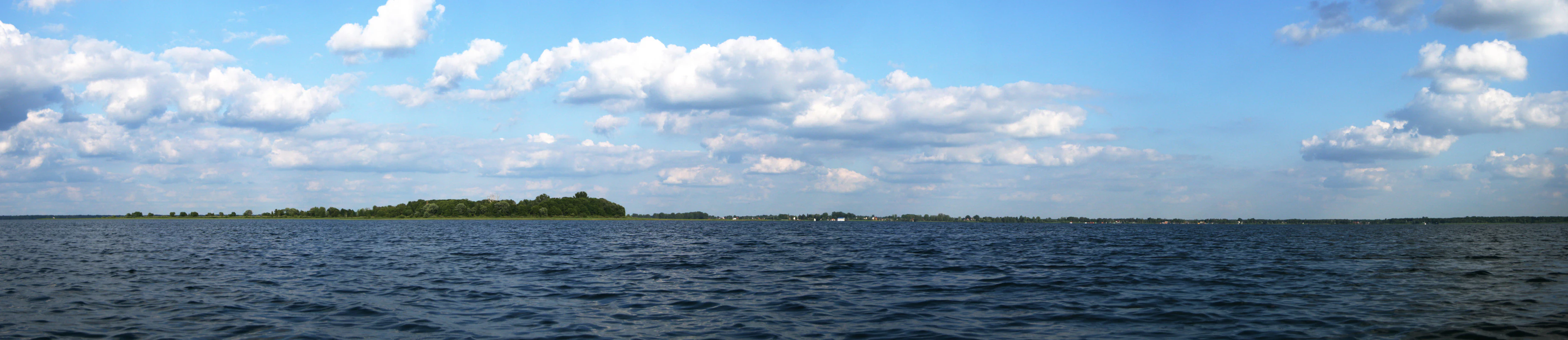 Panoramic view of a large lake with a small forested island under a partly cloudy sky