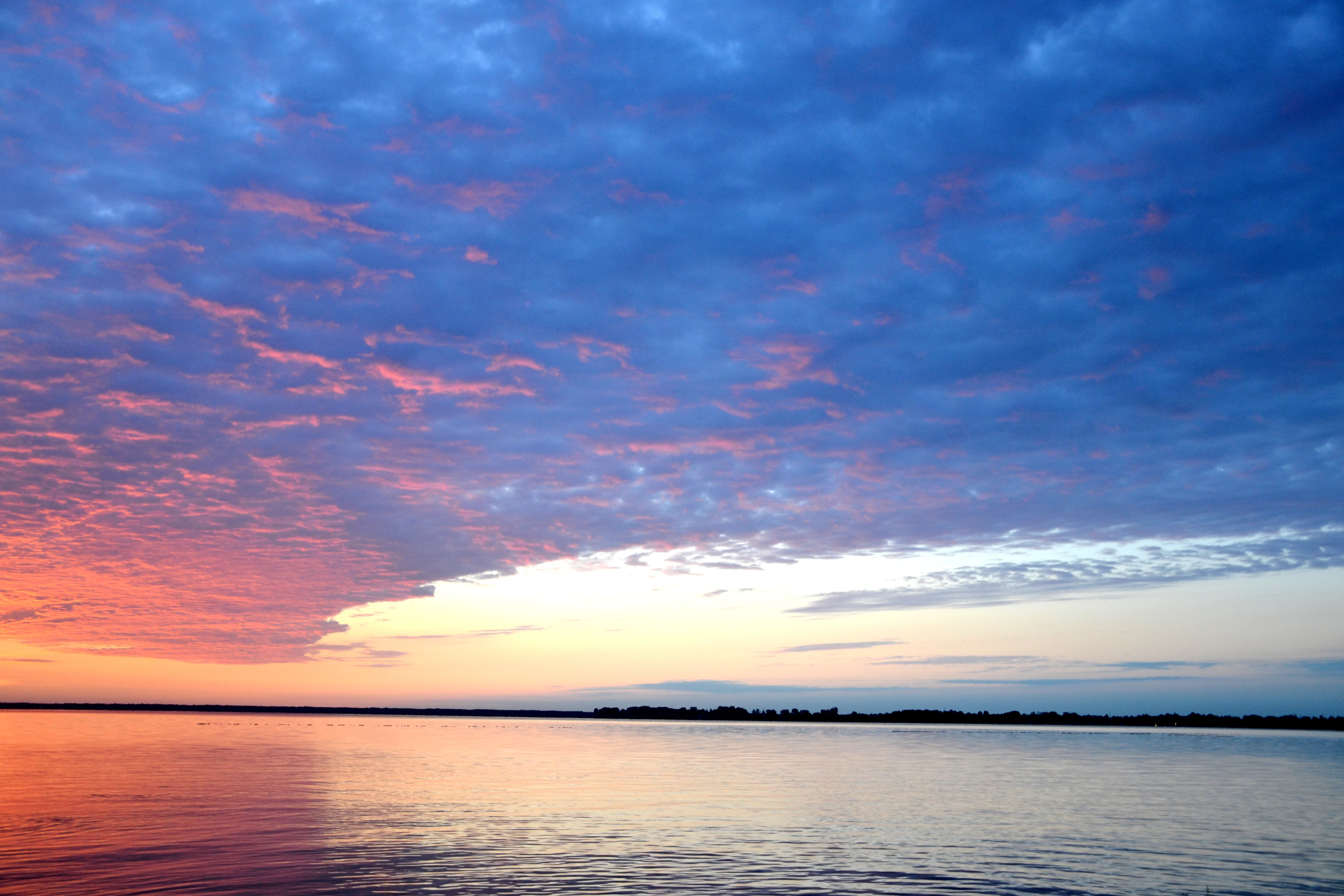 Calm lake surface reflecting colorful sunrise sky with pink, orange, and blue clouds