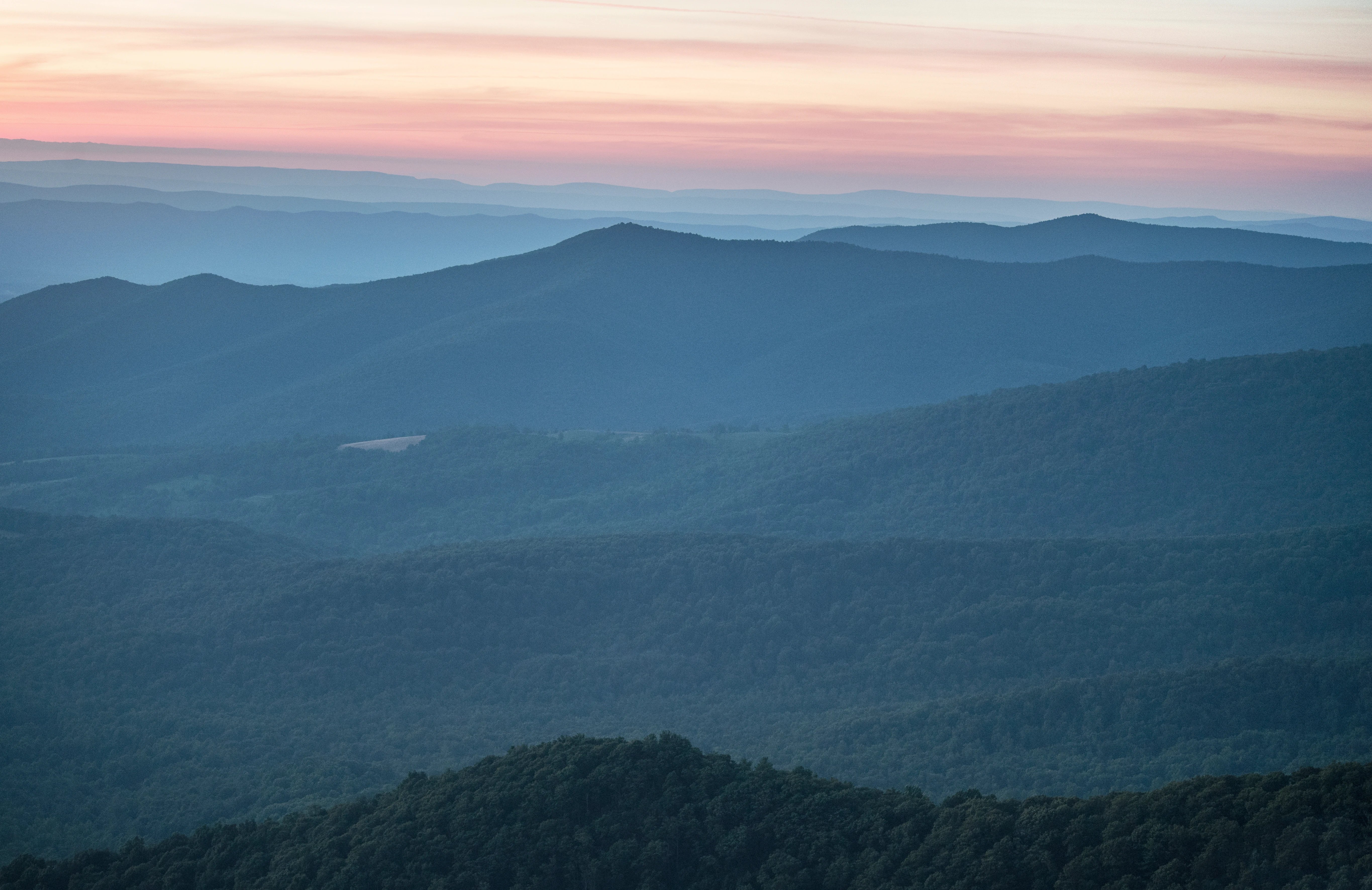 Sunset sky with pink and orange hues over layered mountain ridges covered in dense forest