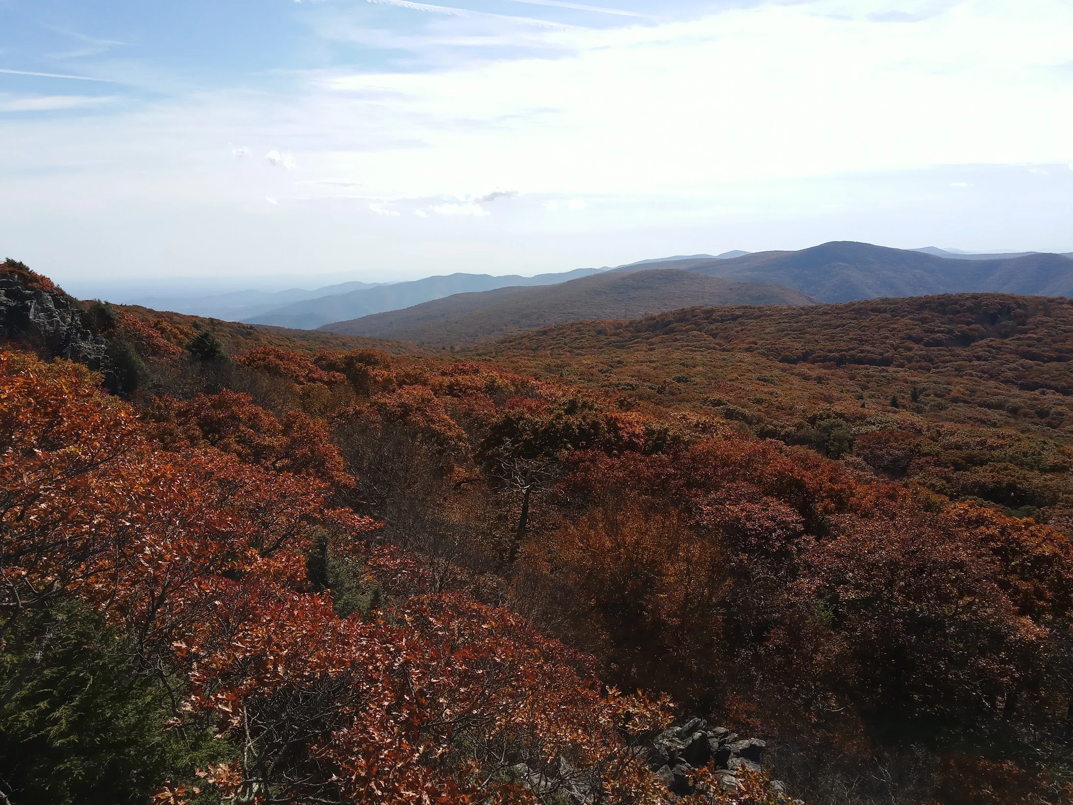 A mountain landscape with autumn-colored trees on hillsides under a partly cloudy sky