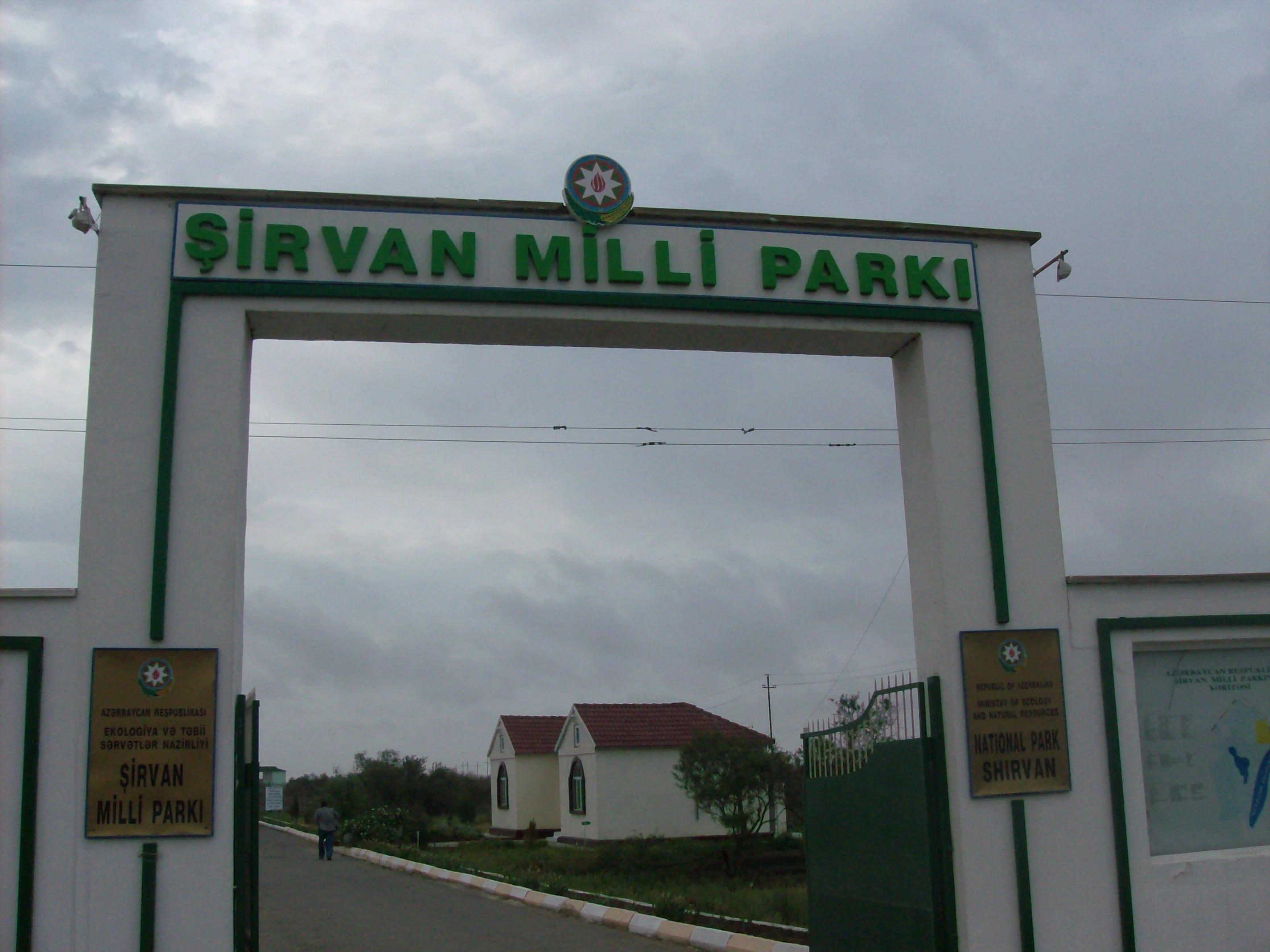 Una gran entrada de arco de hormigón con texto verde que dice Sirvan Milli Parki, enmarcada contra un cielo nublado.