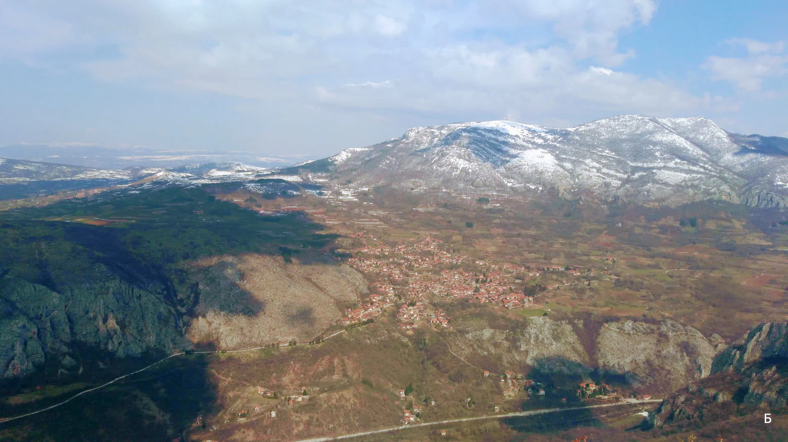 Aerial landscape view of Sićevo Gorge with mountainous terrain, a valley containing a village, and snow-capped peaks under a partly cloudy sky