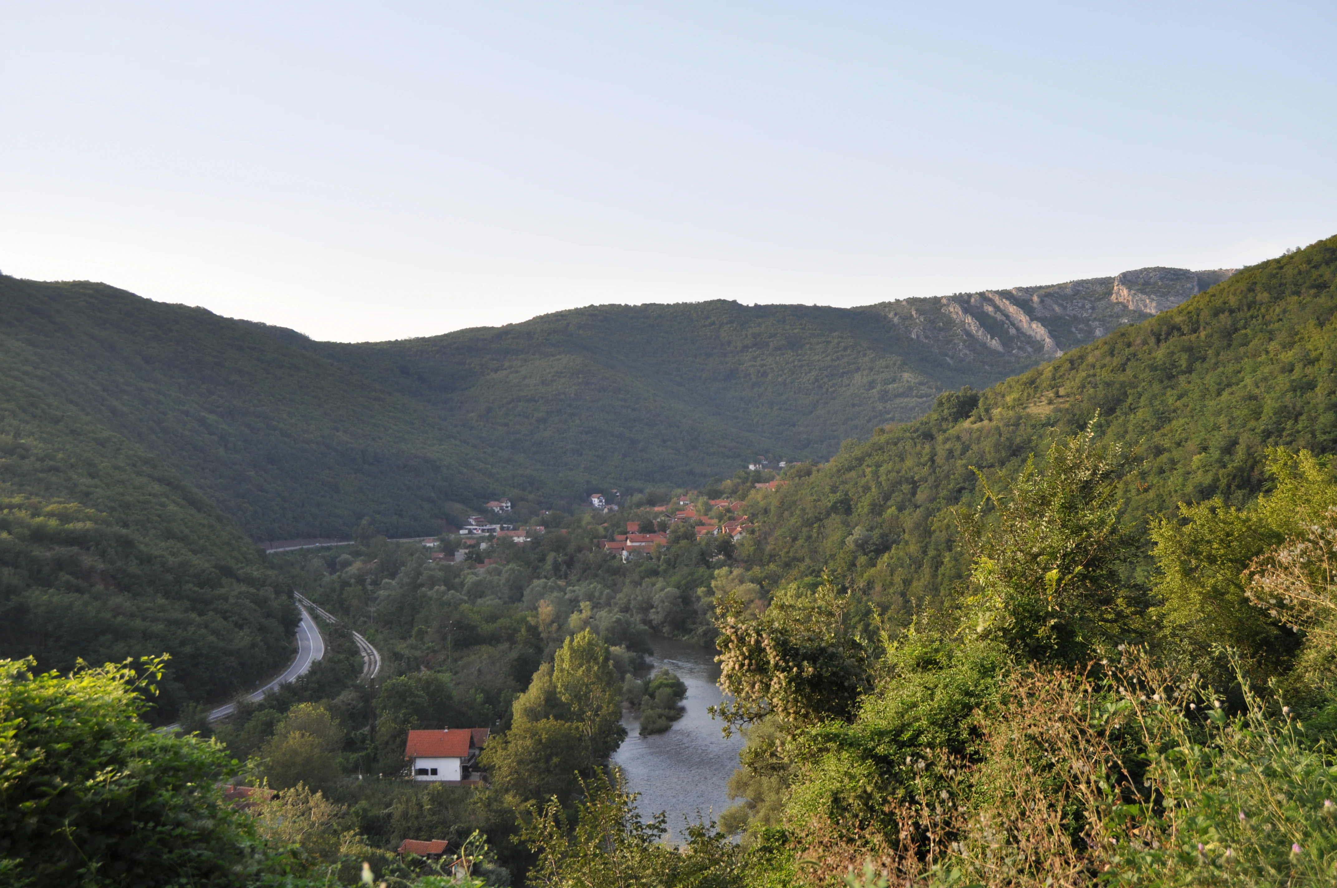 Panoramic view of Sićevo Gorge entrance showing the Nišava River, green hills, a winding road, and Prosek settlement with a red-roofed building