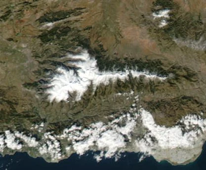 Satellite image of Sierra Nevada mountain range with snow-covered peaks, surrounding hills, and the Mediterranean Sea