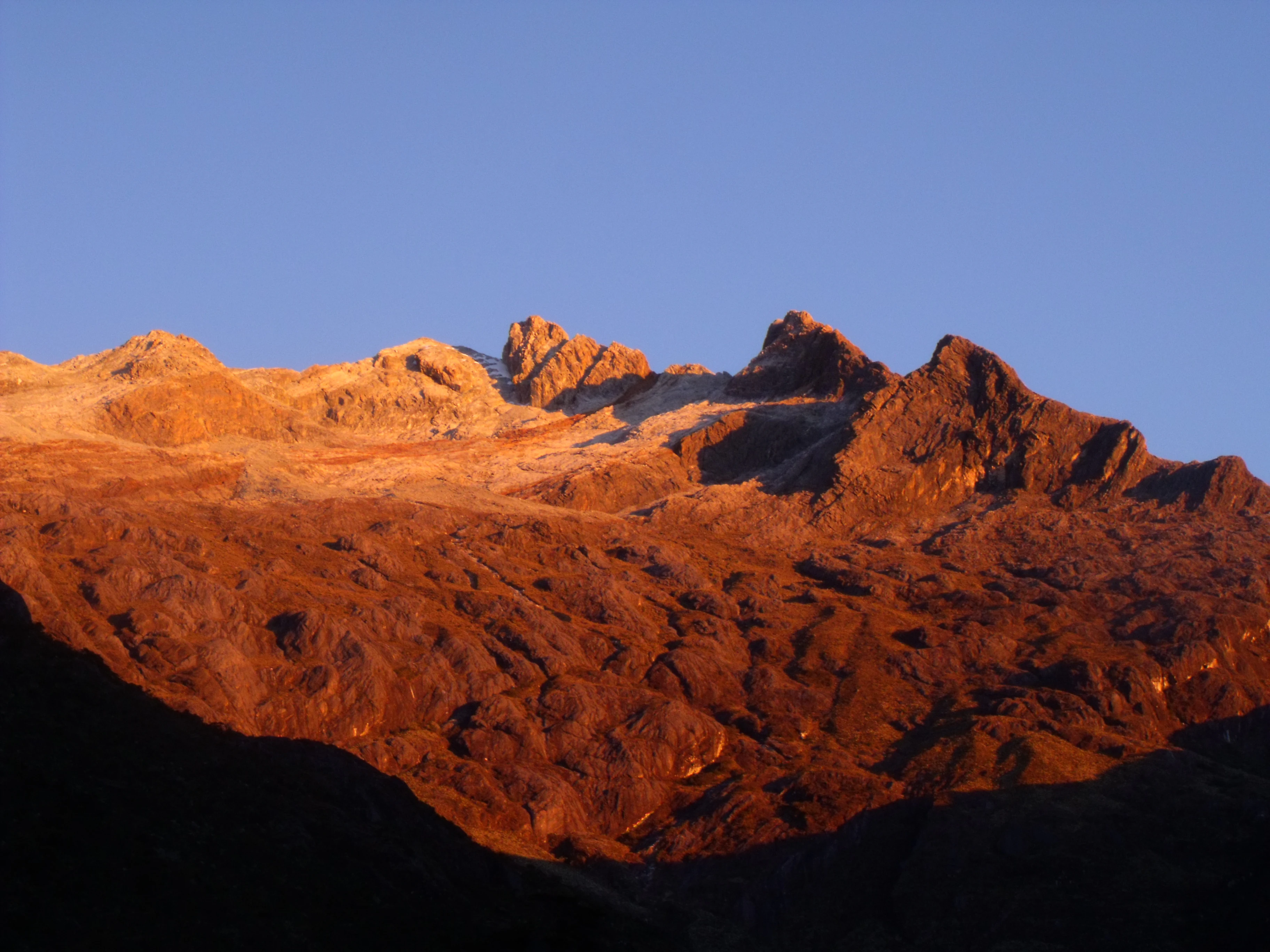 Cimas de montañas rocosas iluminadas por cálida luz solar bajo un cielo azul despejado