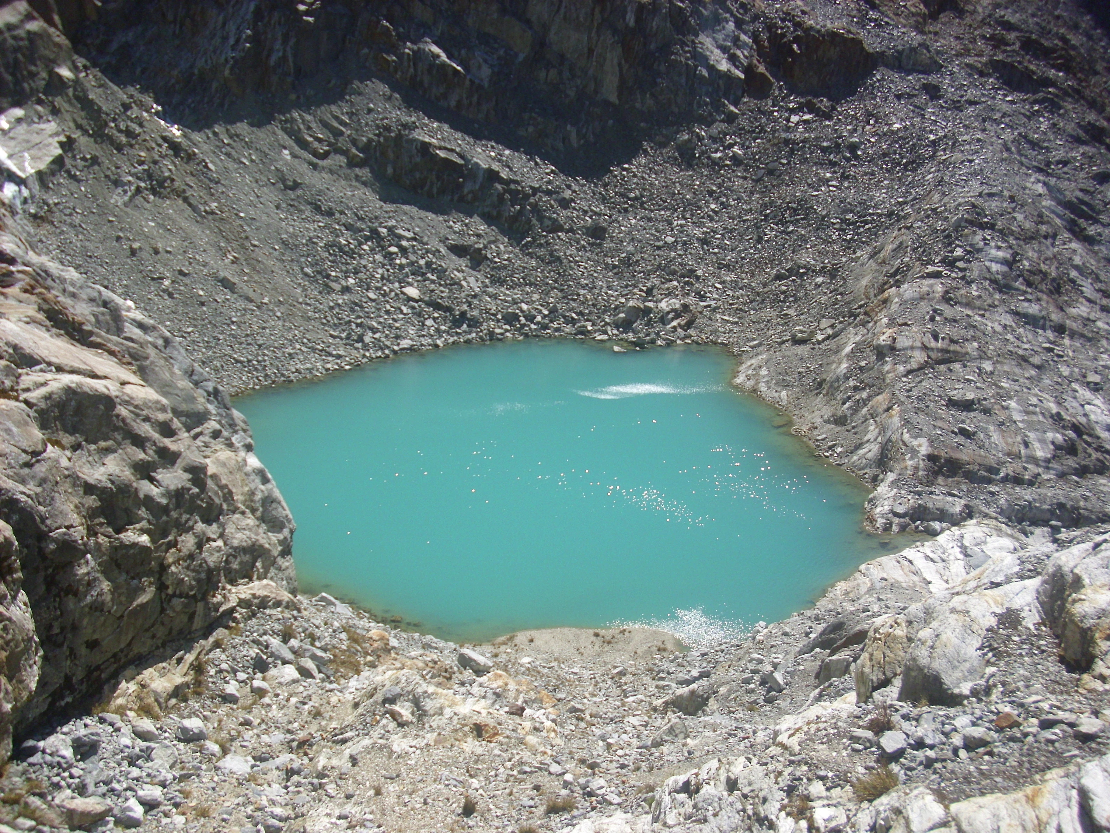 A turquoise lake nestled between rocky mountain slopes with boulders in the foreground