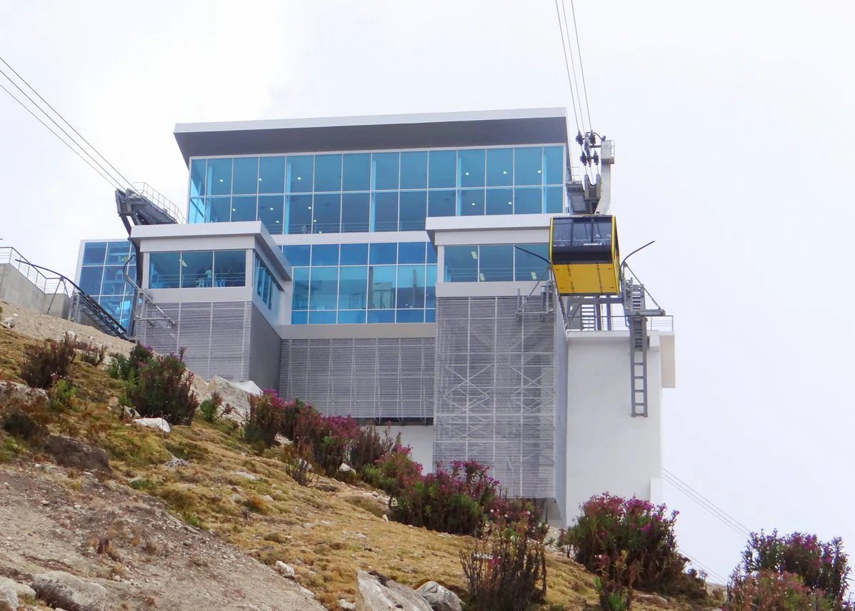 Estación moderna de teleférico con grandes ventanales y teleférico amarillo en una ladera de montaña