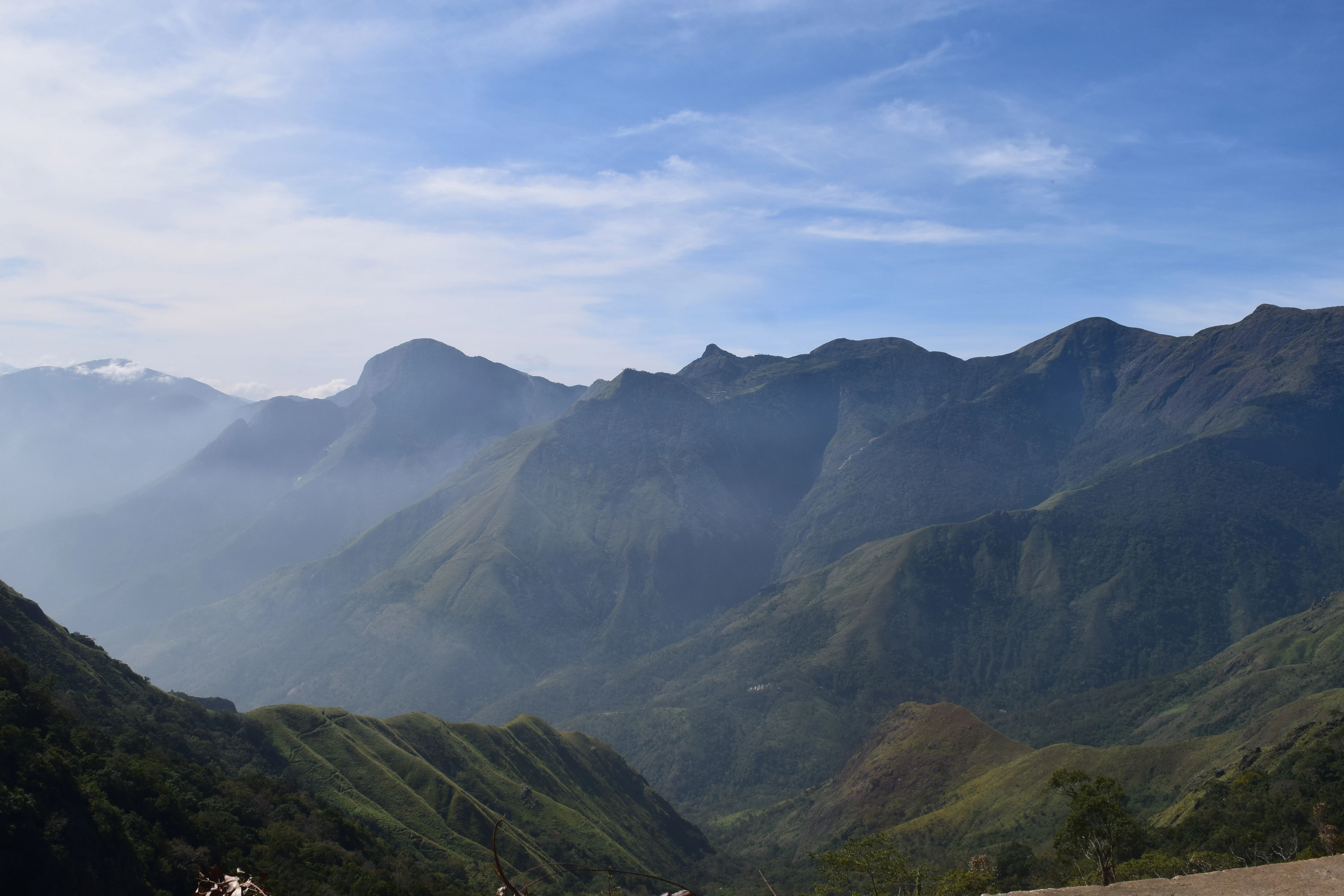 Wide view of mountainous landscape with valleys, green slopes, and distant peaks under a partly cloudy sky