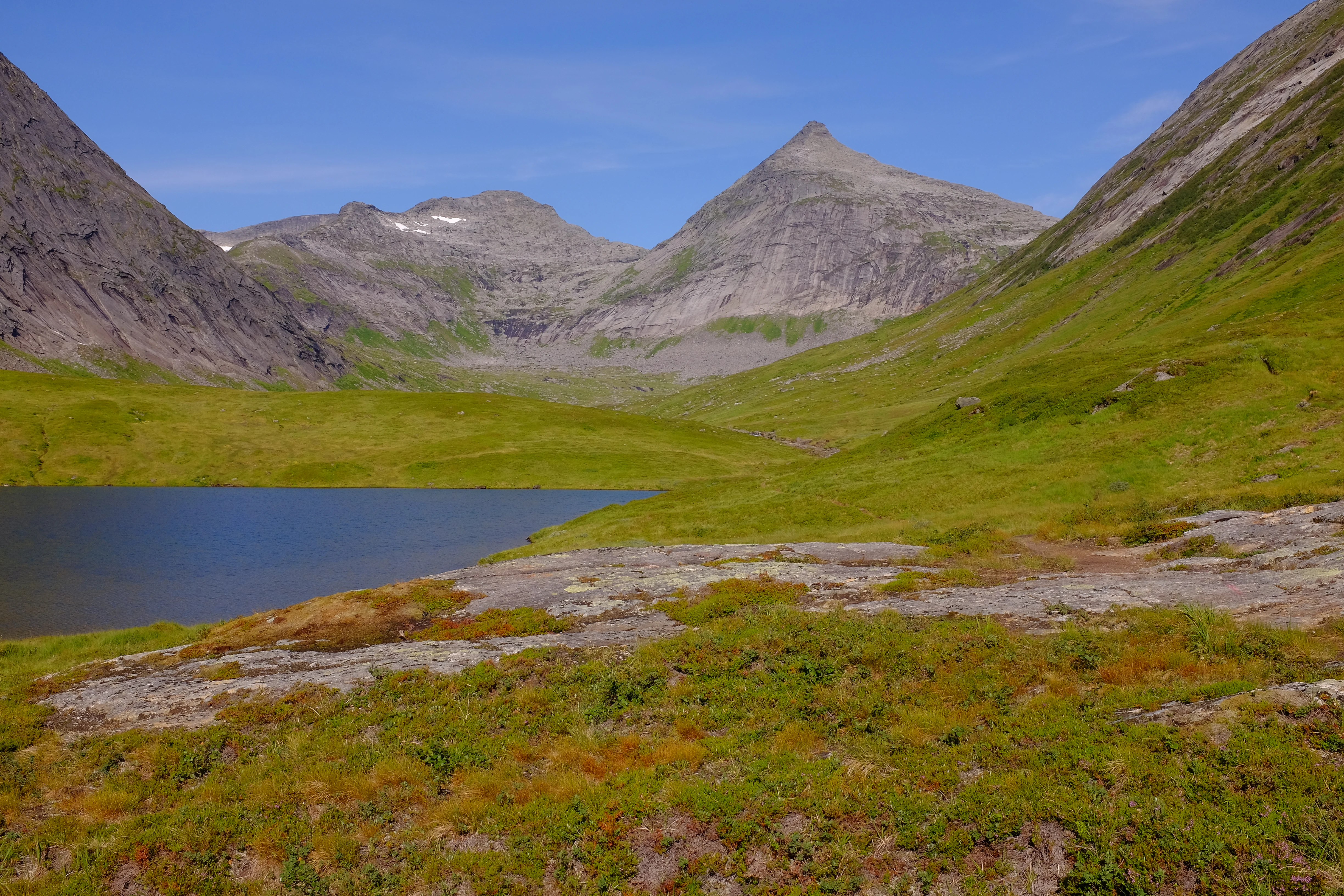 Mountain landscape with a lake, green valley, and rocky peaks under a clear blue sky