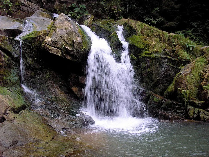 Waterfall flowing over moss-covered rocks into a pool surrounded by green vegetation