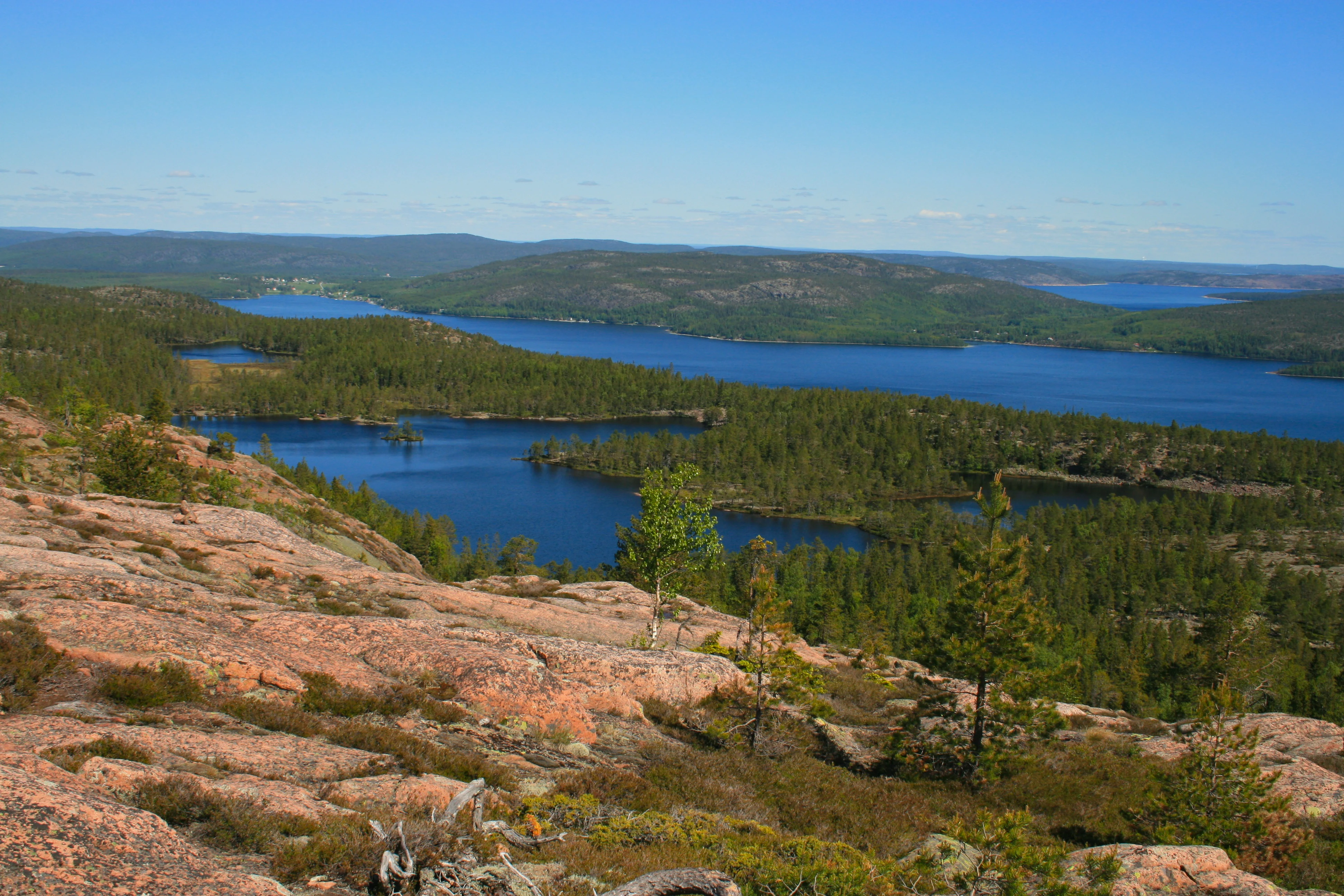 Panoramic landscape view with rocky terrain, blue lakes, and forested hills under a clear blue sky