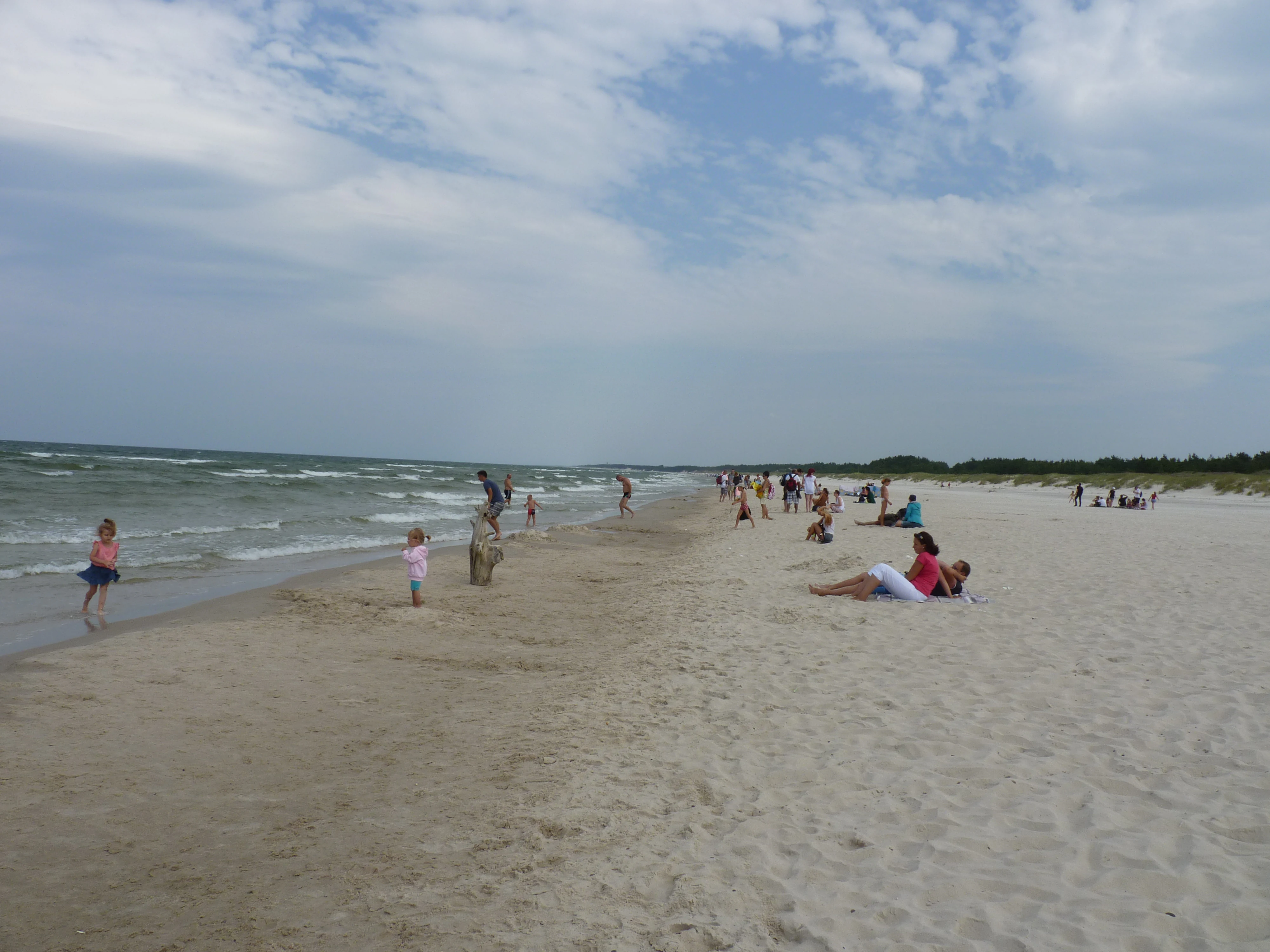 Sandy beach with people relaxing near the sea under a partly cloudy sky