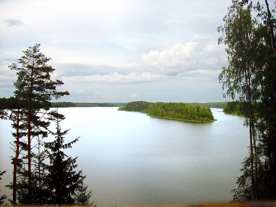 A wide view of Lake Sapsho showing forested islands surrounded by calm water with trees in the foreground and a cloudy sky