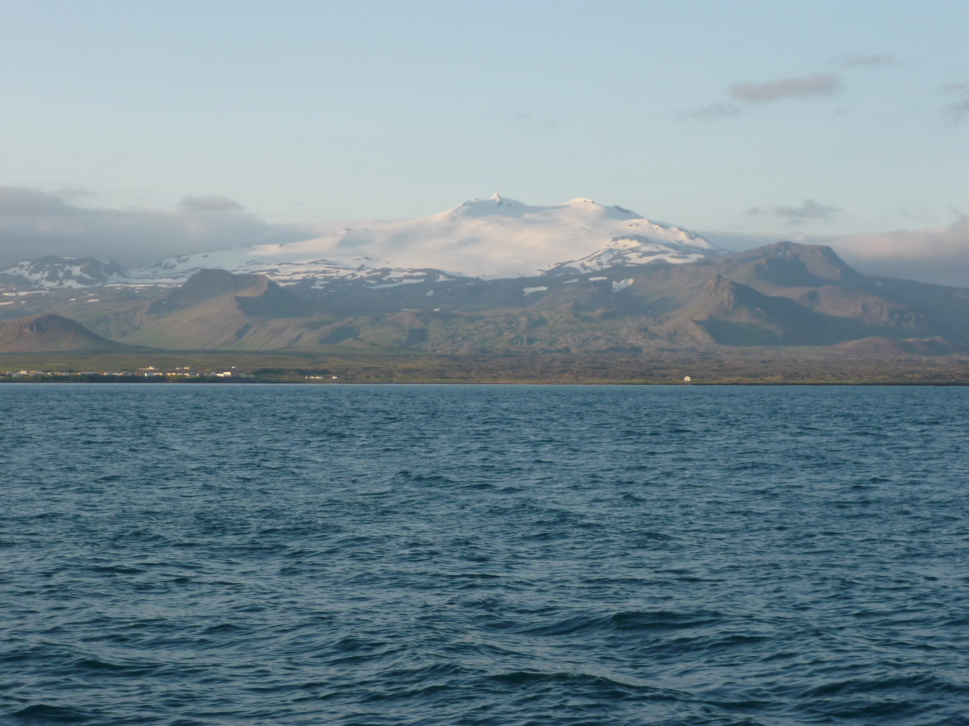 Distant snow-capped mountain with glacier visible across a body of water under a partly cloudy sky